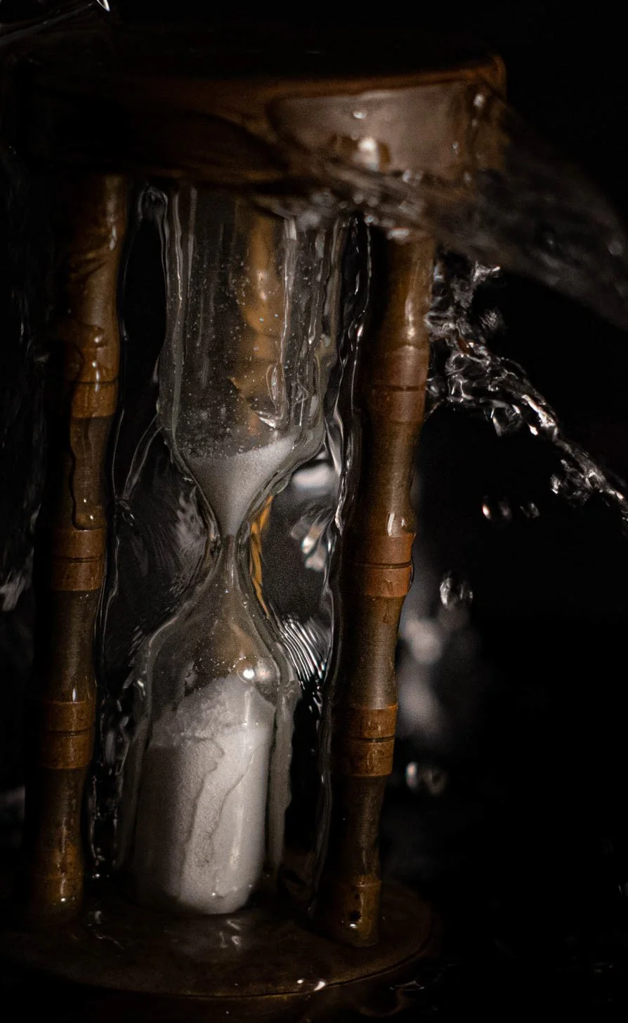 A close-up image showing a melting wax candle under a running faucet of water, with the water flowing over the candle and creating a glossy, reflective surface.