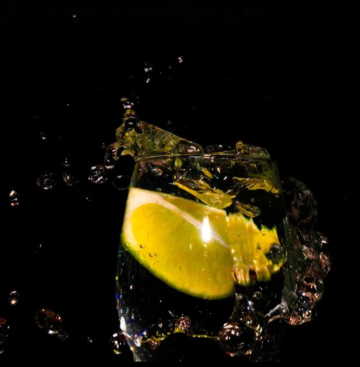 A glass of water with lemon slices and ice, splashing on a black background.