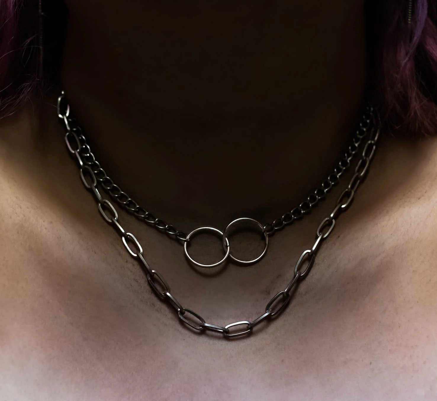 Close-up of a person's neck wearing two layered silver chain necklaces with circular link patterns.