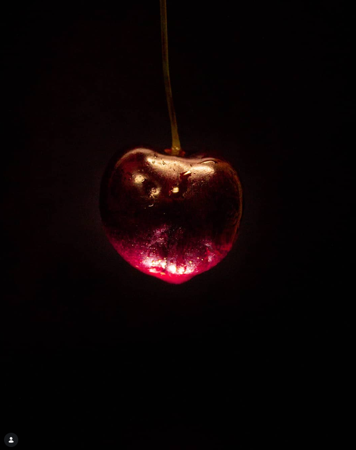 A cherry with a glowing bottom illuminated from below, set against a black background.