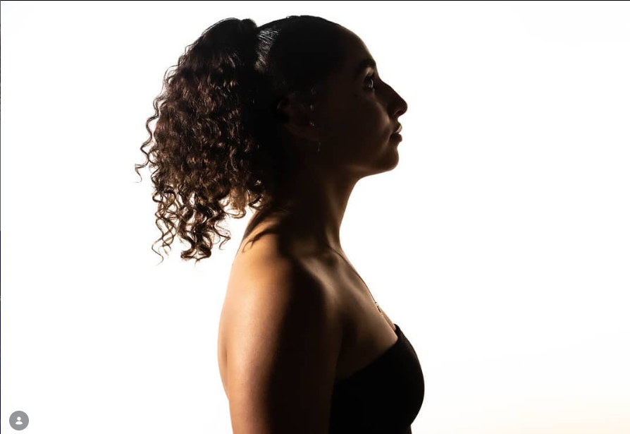 Silhouette of a woman with curly hair, facing right, against a bright white background.