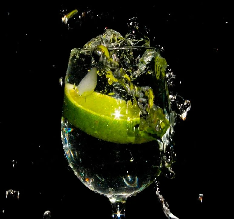 A lime wedge dropped into a glass of clear water against a black background, creating a splash with bubbles.