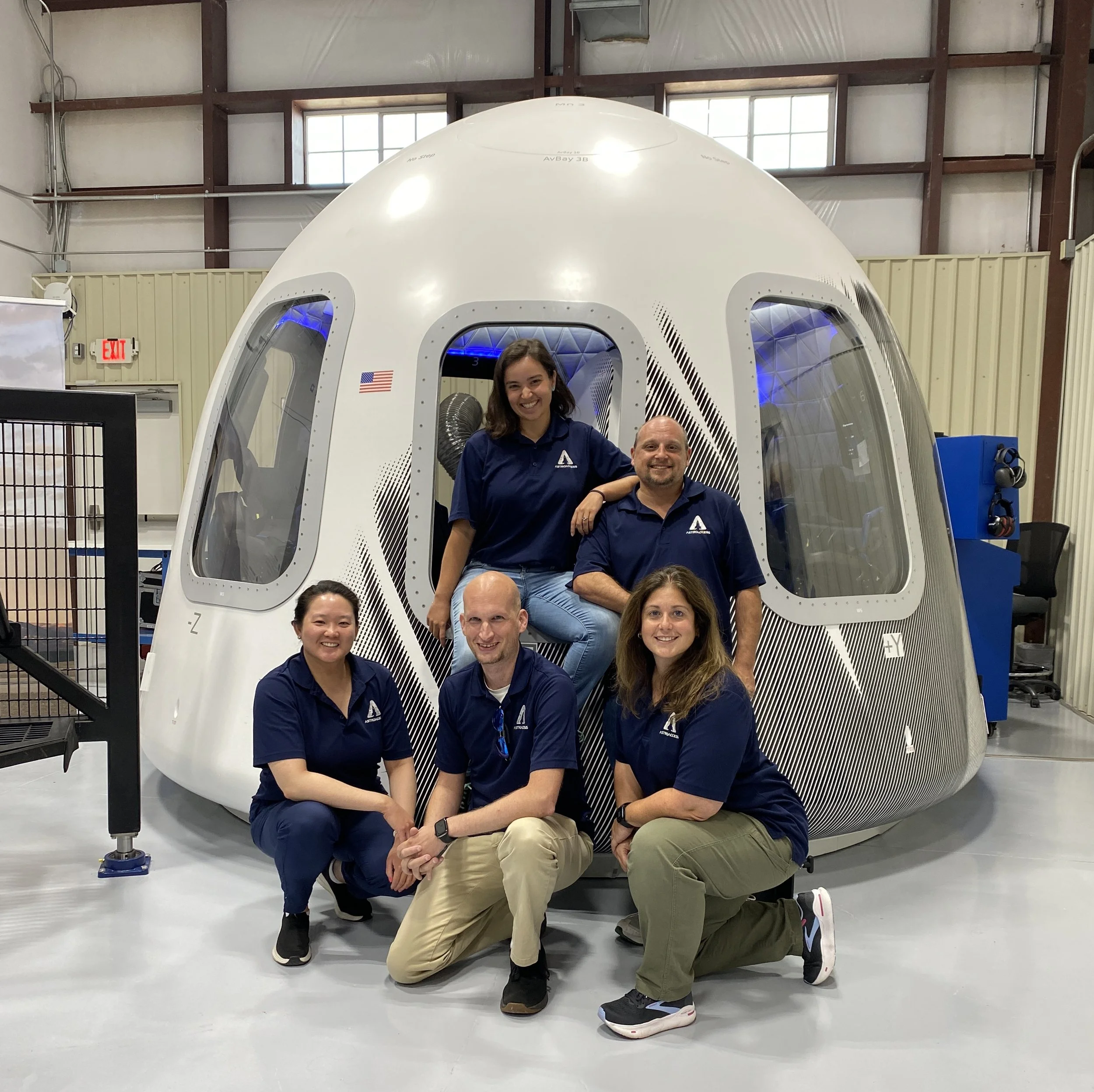 AstroAccess team members wearing blue AstroAccess polos stand in front of the Blue Origin New Shepard space capsule mock-up.