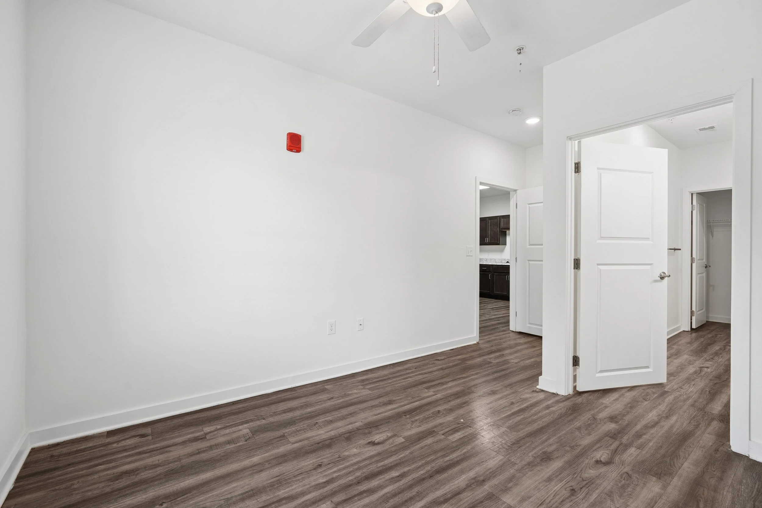 Empty room with white walls, wood flooring, ceiling fan, and open closet doors.