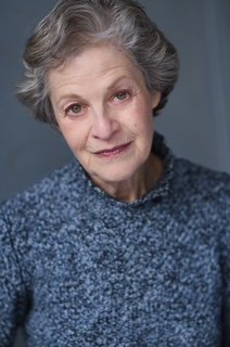 A woman with gray hair, wearing a blue sweater, looking at the camera with a slight smile.