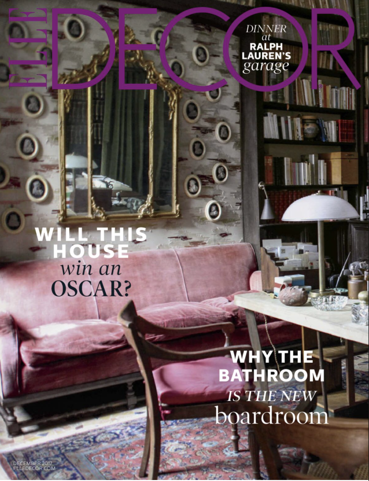Interior of a living room with a pink velvet sofa, a wooden armchair, a table with decorative items, a bookcase, a mirror with a gold frame, and a wall with small round frames. Cover of Elle Decor magazine with headlines about house decor, Oscars, and bathroom renovation.