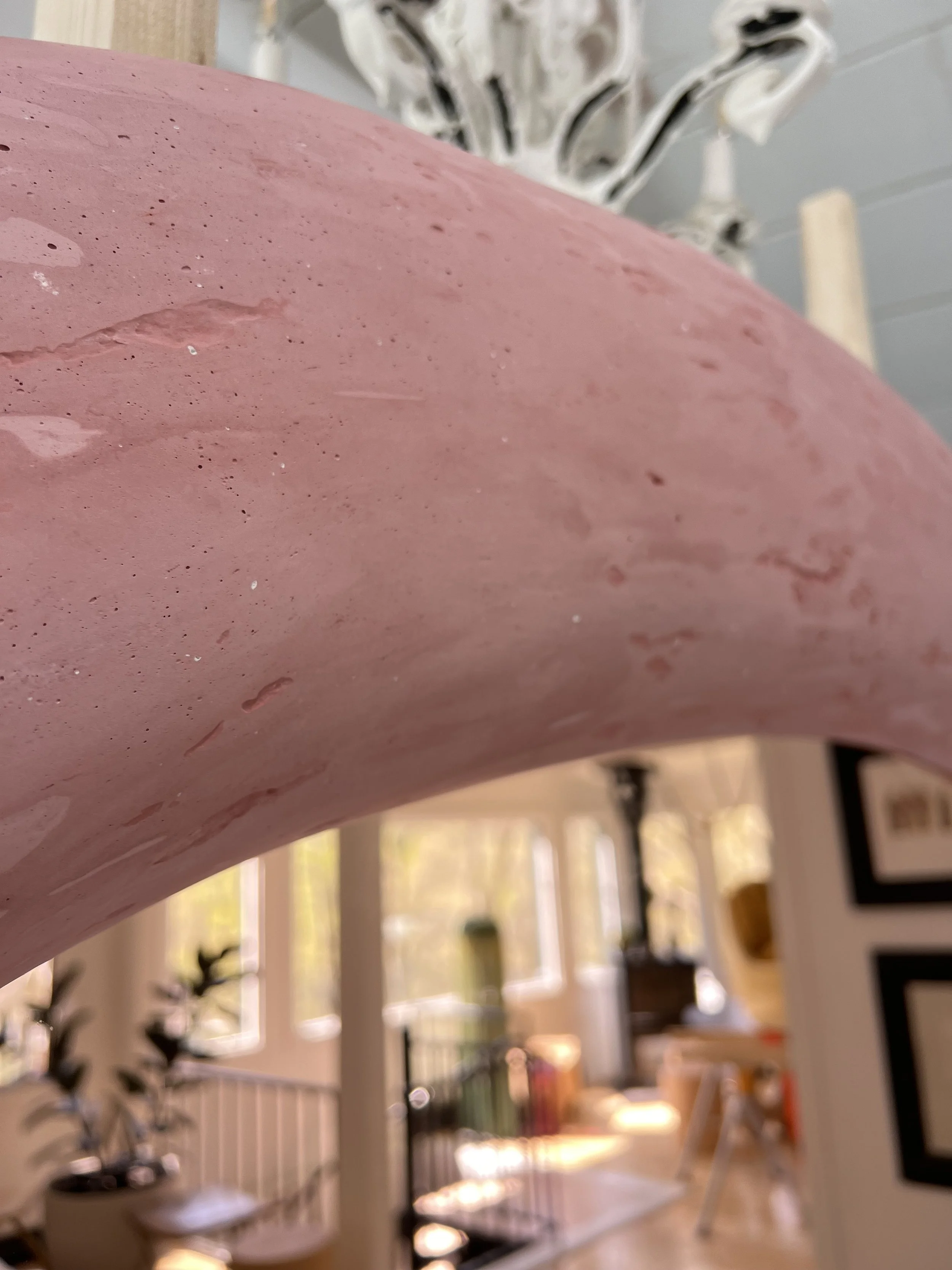 Close-up of a pinkish marble or stone surface with a speckled pattern, part of a table or countertop, in an indoor setting with blurred background including framed pictures, window, and furniture.