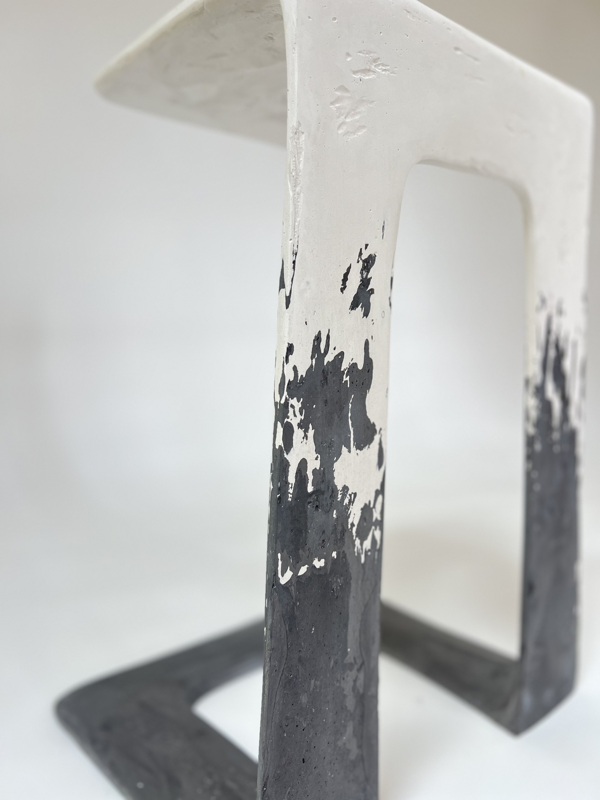Close-up of a metallic letter 'L' with a distressed black and white paint design, mounted on a white wall.