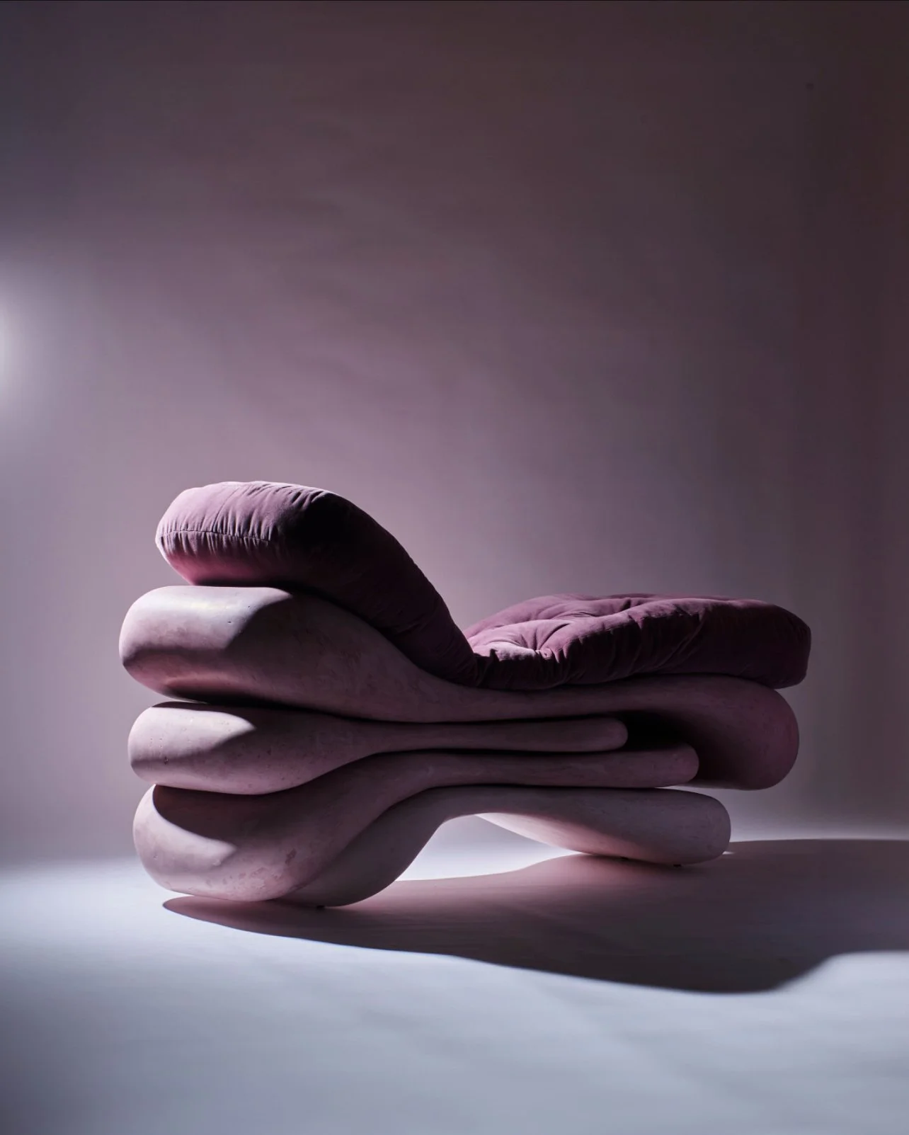 A unique stack of smooth, oval-shaped rocks with soft, purple velvety cushions on top, set against a neutral background with dramatic lighting.