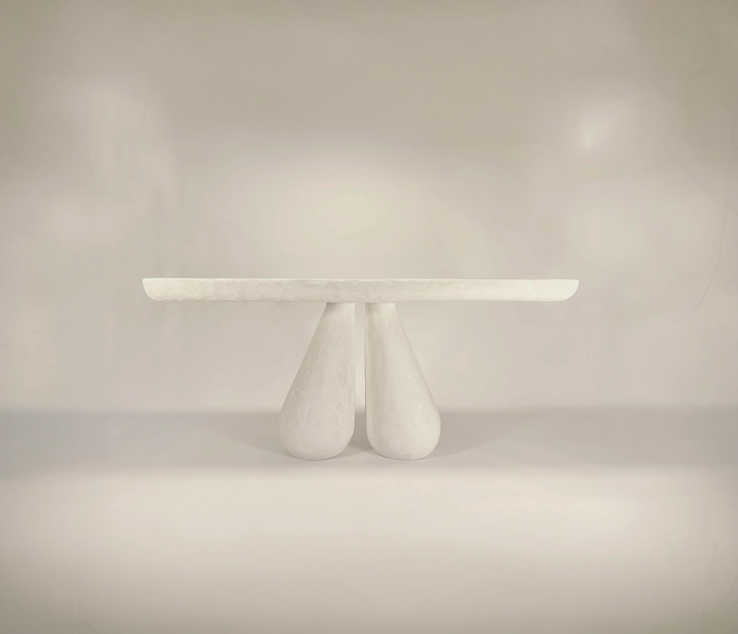 A minimalist, white ceramic pedestal or bowl with a smooth, rounded edge, set against a plain light-colored background.