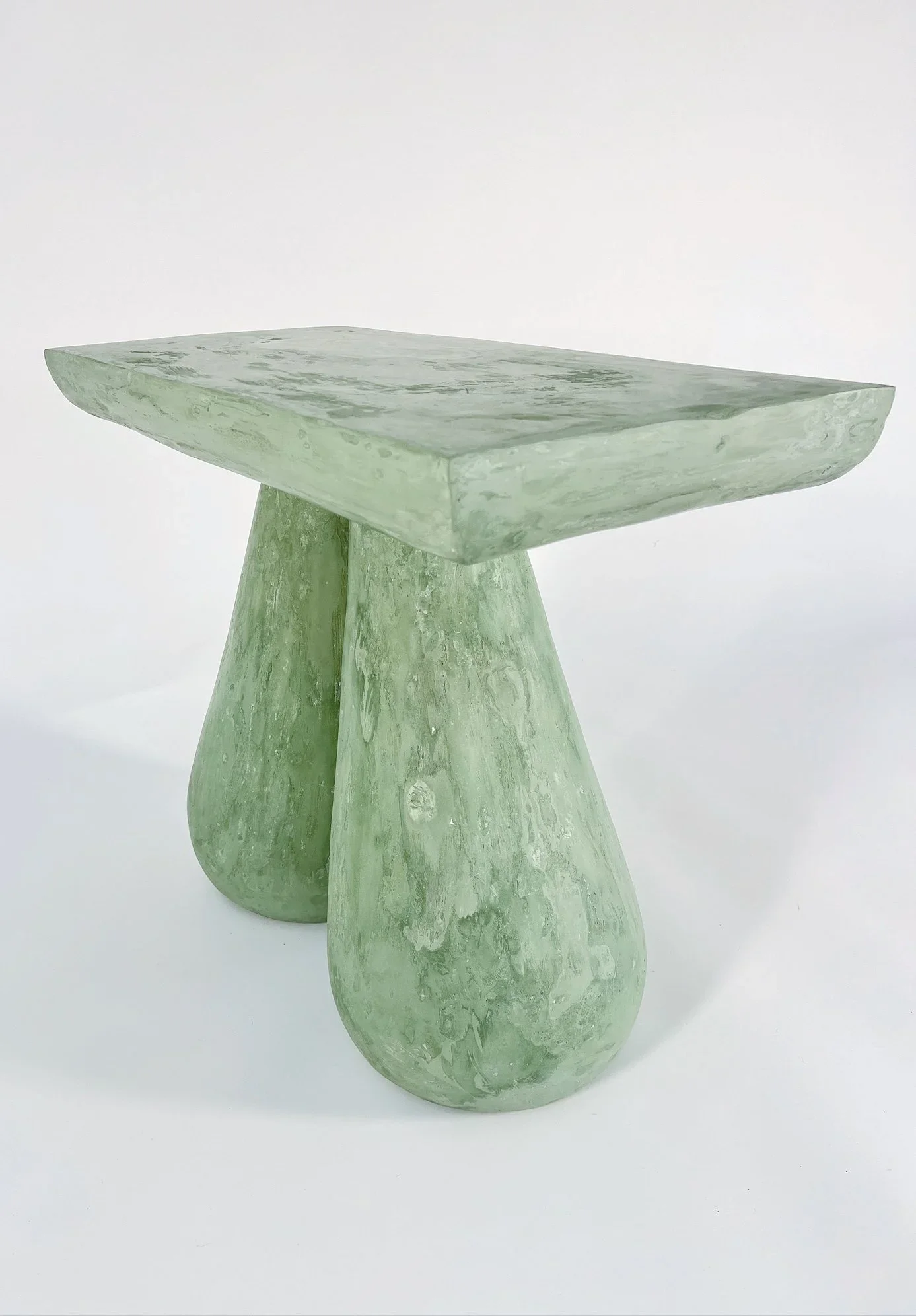 A sculptural table made of green marble with a rectangular top and curved, rounded legs.