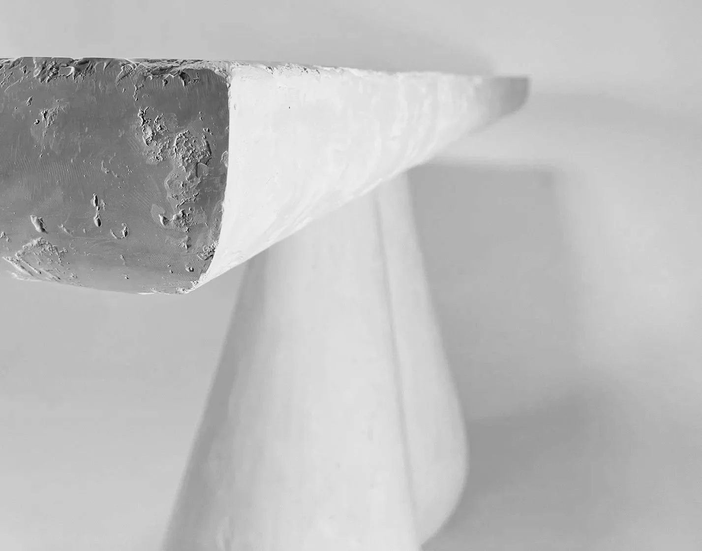 Black and white close-up view of a modern pendant light fixture with a textured, uneven surface and smooth, elongated shape.