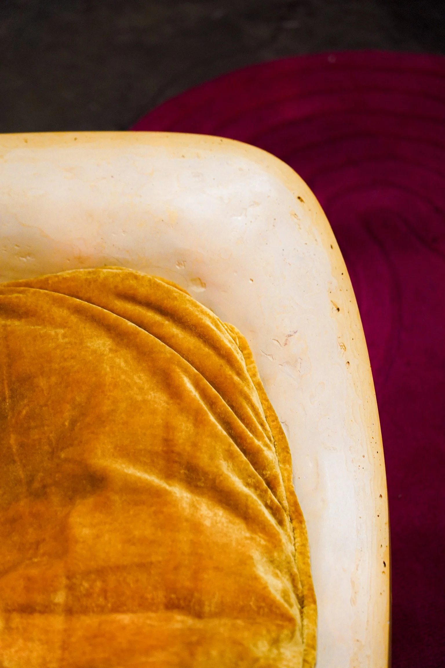 Close-up of a stack of crispy, golden-brown tortilla chips in the foreground. In the background, there are slices of onion with purple skin and white flesh. The surface appears to be a dark, textured surface.