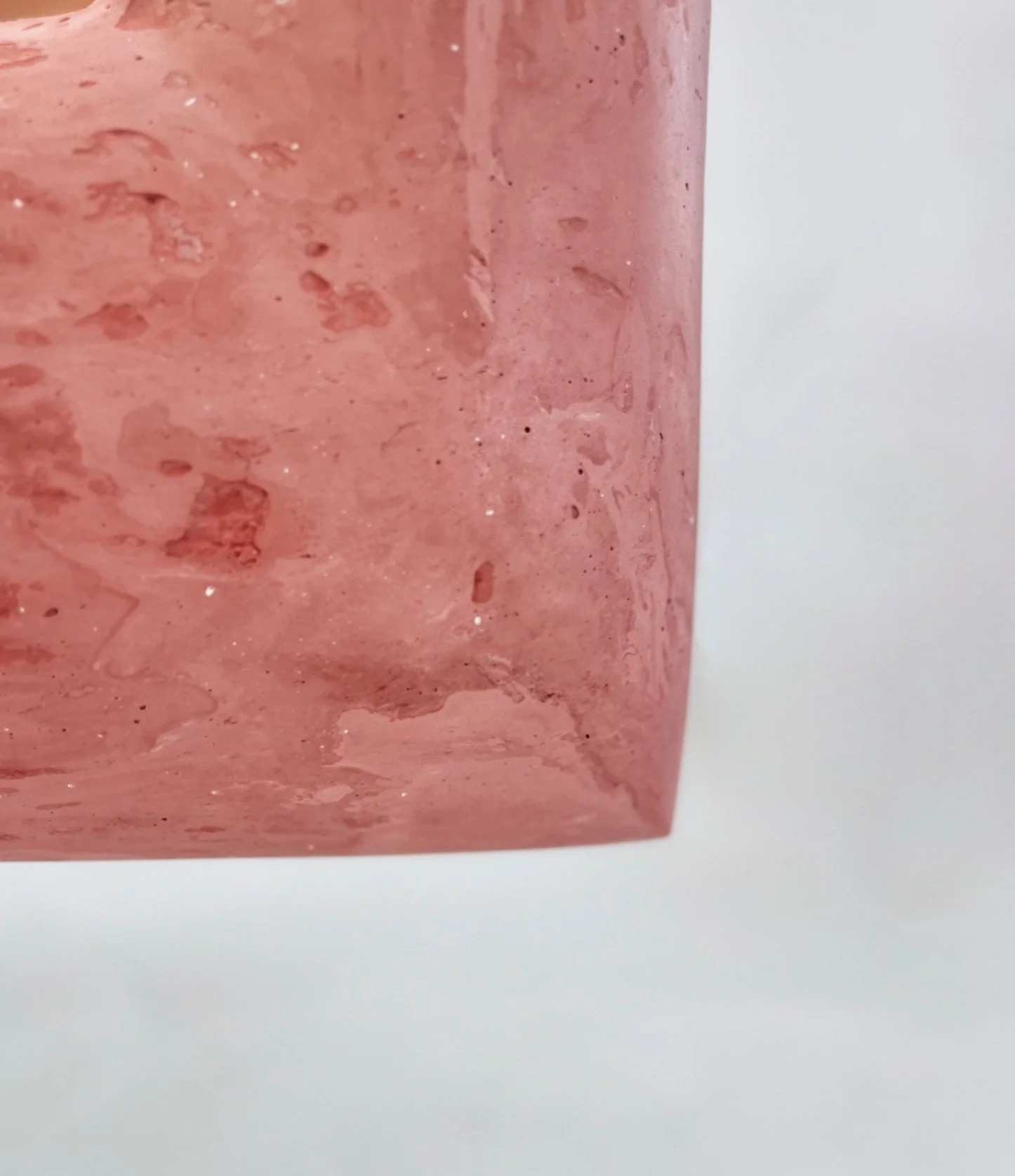 Close-up of a pink, textured soap bar with a slightly rough surface and small sparkles, resting on a white surface.