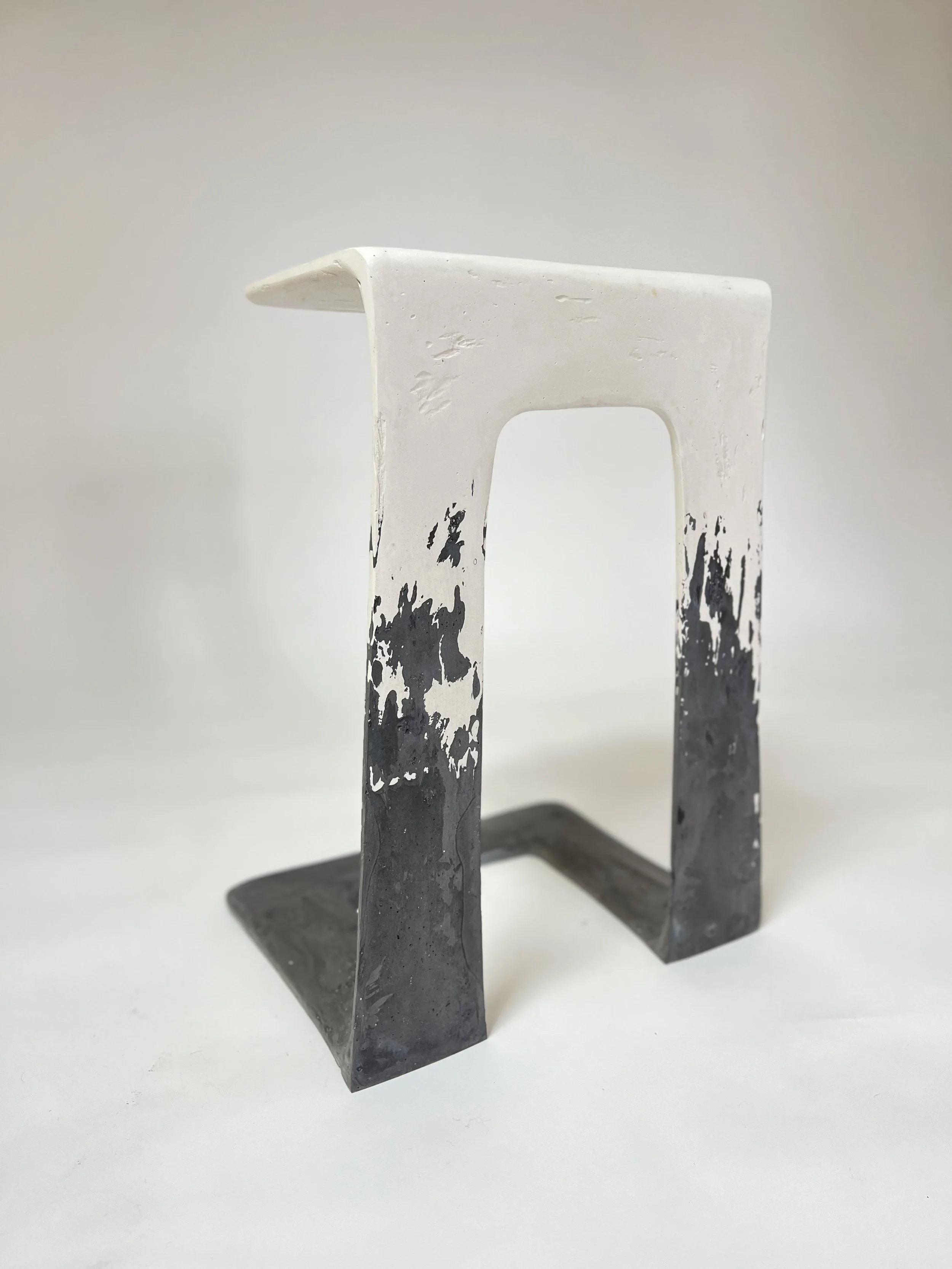 A metallic sculpture with two black and white striated vertical elements connected by a horizontal base, taken against a plain white background.