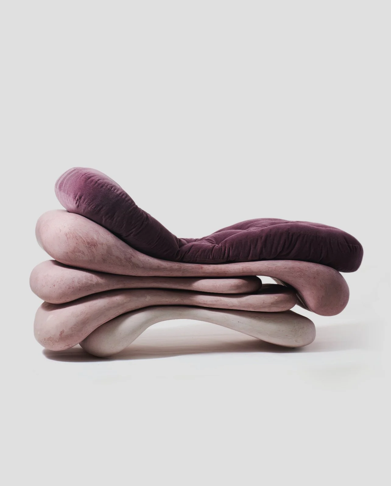 Artistic lounge chair with a layered, organic design, featuring a pinkish base and dark purple cushions.