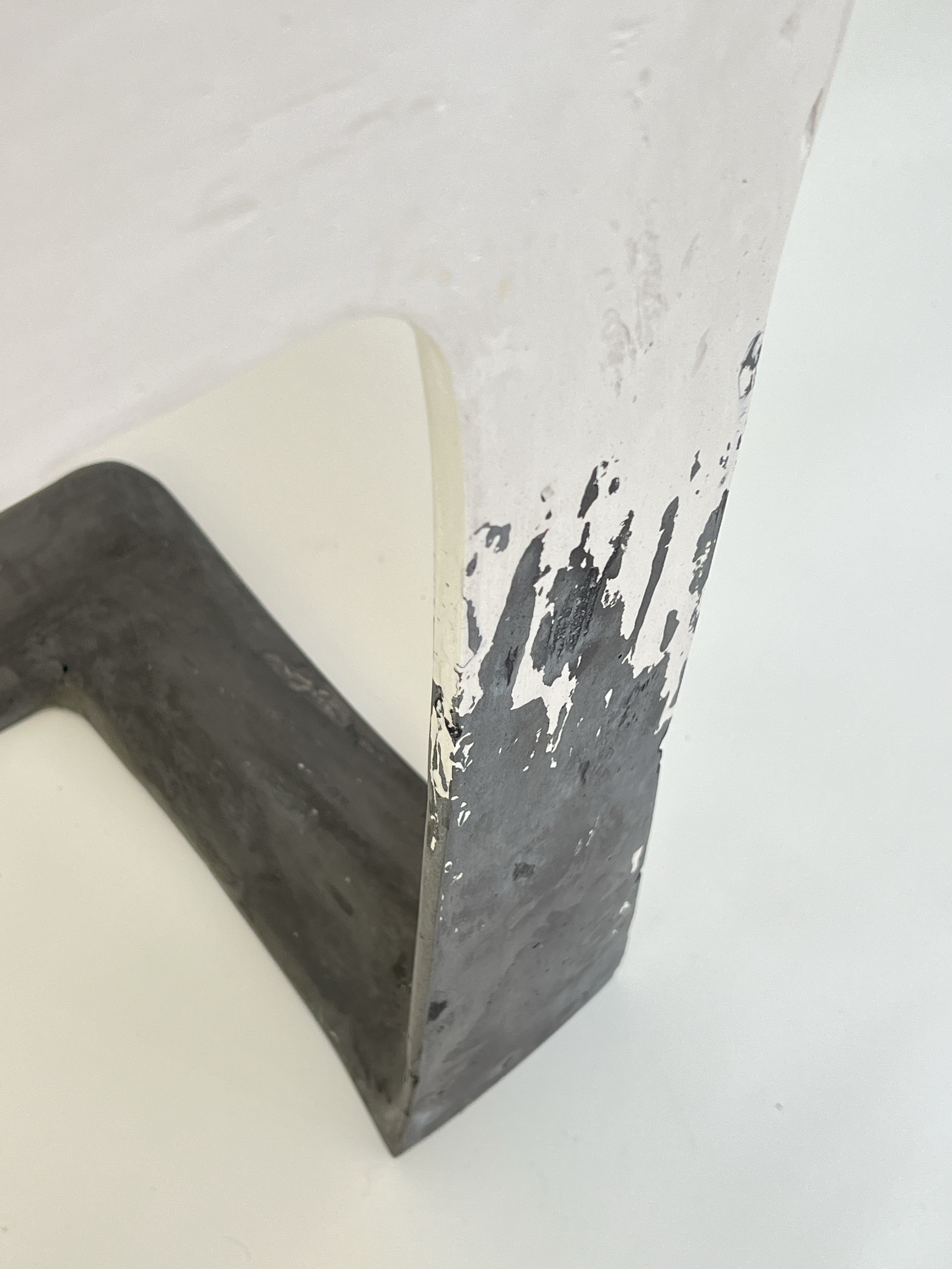 Close-up of a corner of a white structure with black paint splatters and a black and white object in the lower left corner on a white background.