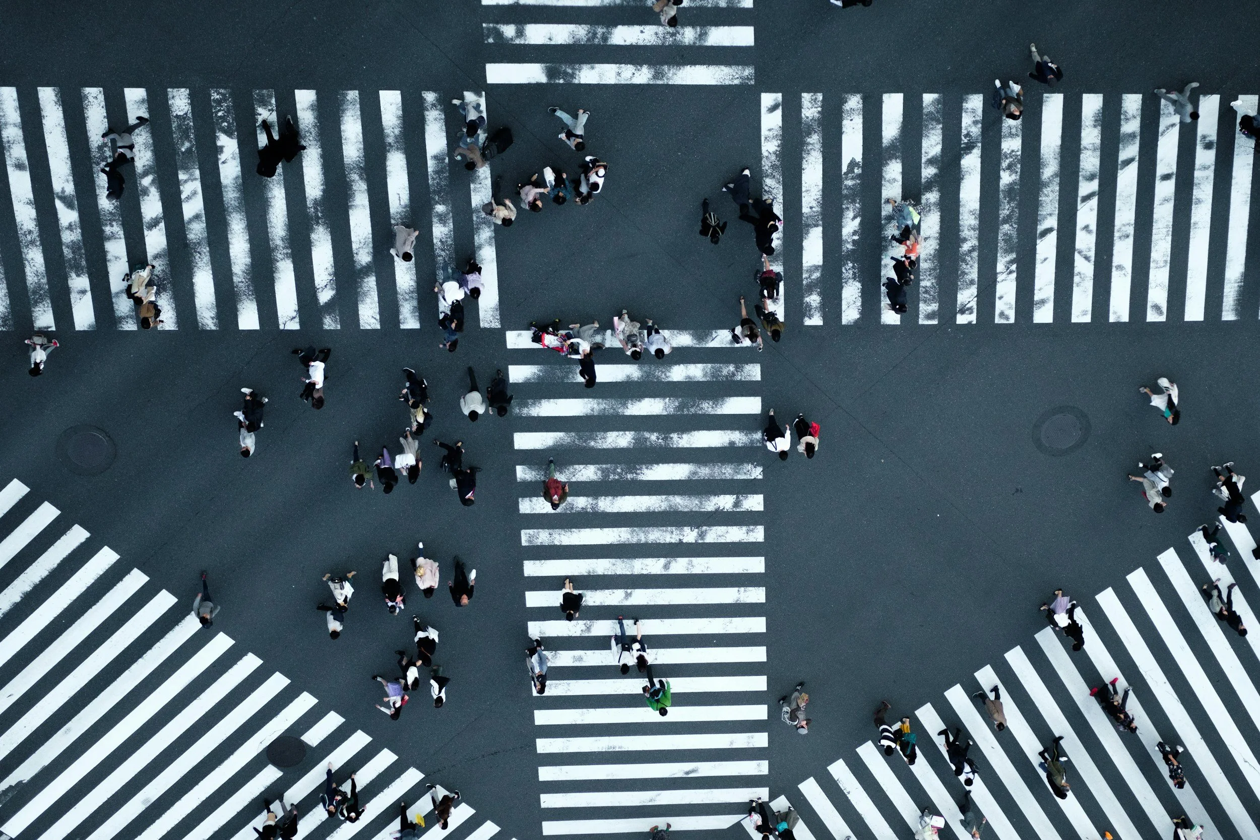 Bird's eye view of a busy crosswalk with pedestrians walking in multiple directions, marked by white striped lines on the road. This is to symbolise the company's name - InterCross Global where we cross paths to change the world.