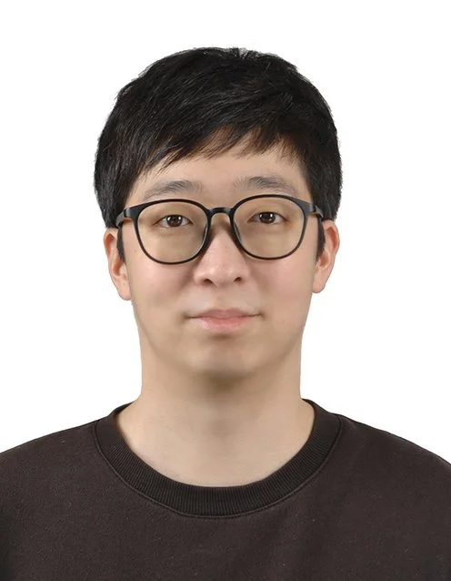 Portrait of the company's founder with short black hair, wearing glasses with a black frame, and a black crew-neck shirt against a plain white background.