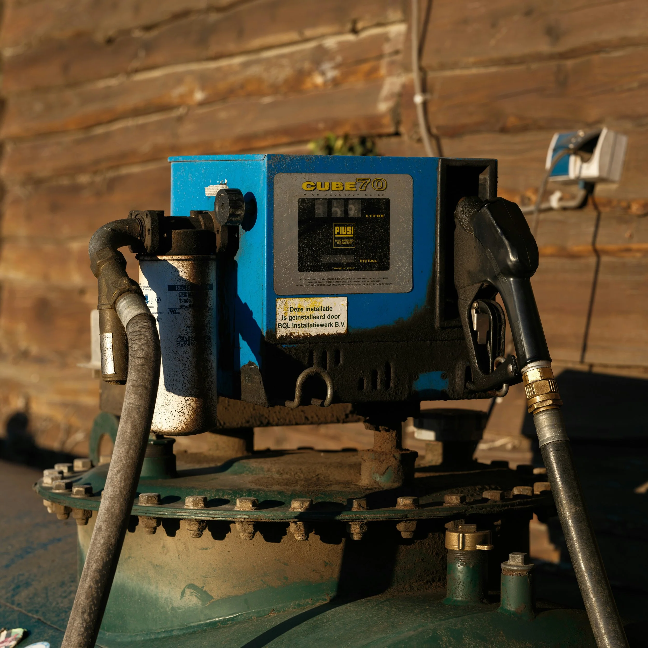 Close-up of a blue high-accuracy meter device with pipes and valves attached, mounted on green equipment, possibly part of an industrial or construction site. The device displays a reading of 151 liters.