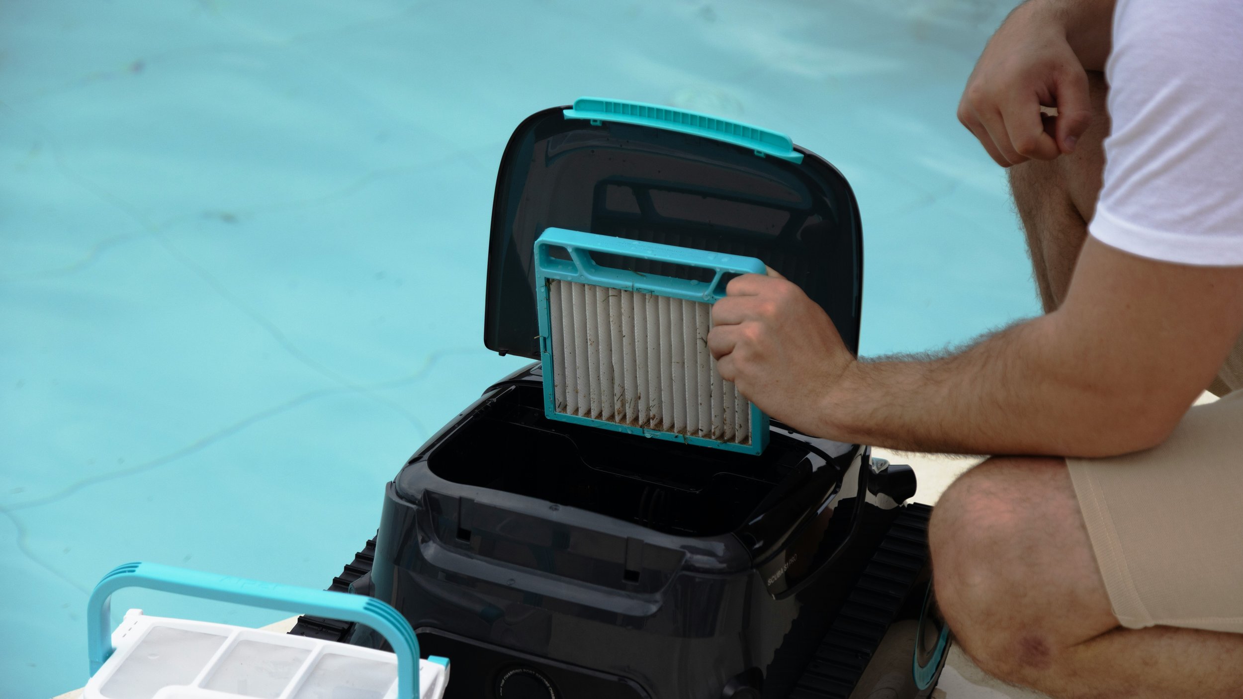 A person cleaning a vacuum filter near a swimming pool.
