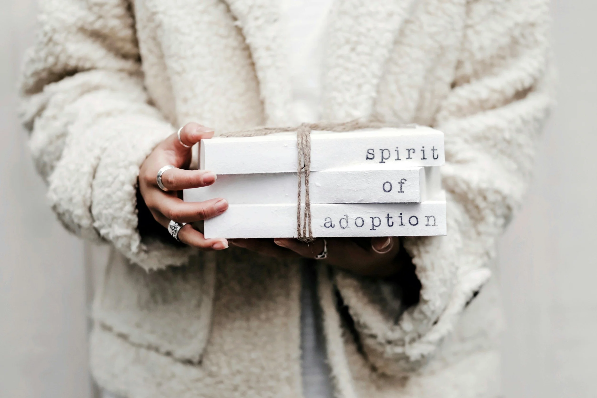 A person wearing a cream-colored fuzzy sweater holding a white box wrapped with twine. The box has text that reads 'spirit of adoption'.