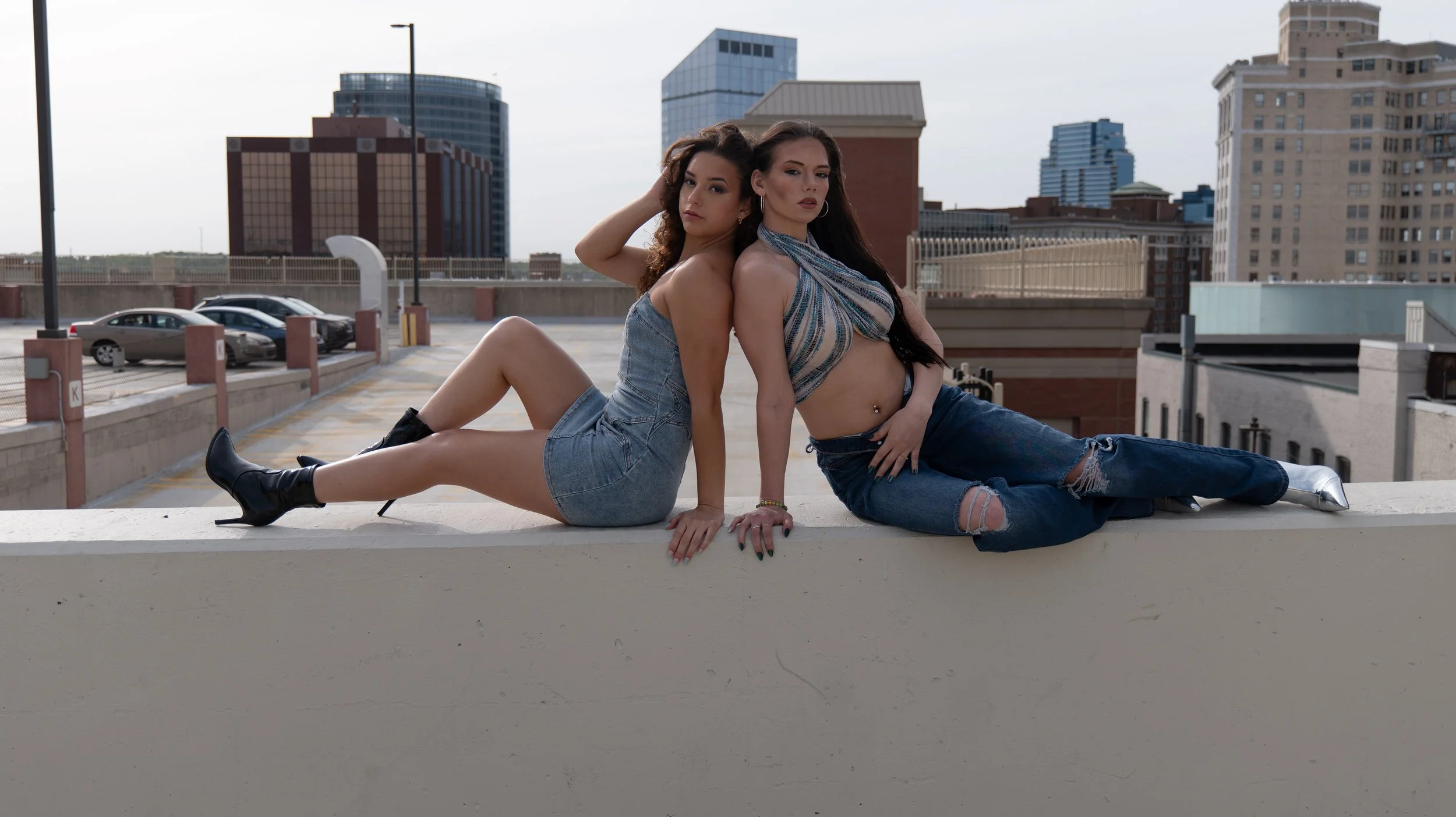 Two women sitting on a rooftop ledge against a cityscape background during daytime.