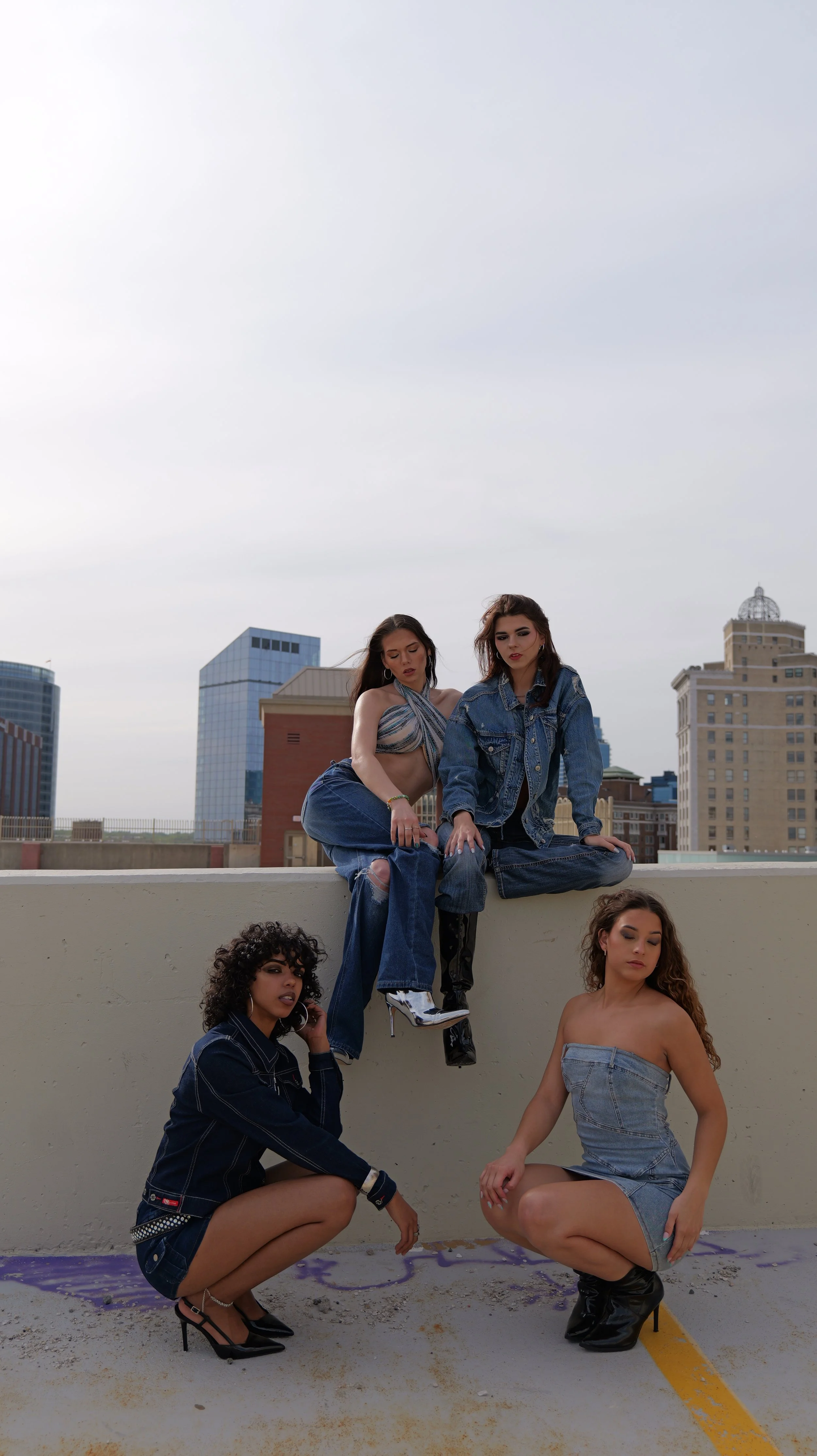 Group of five young female models posing on a rooftop with city buildings in the background, wearing casual and trendy clothing.