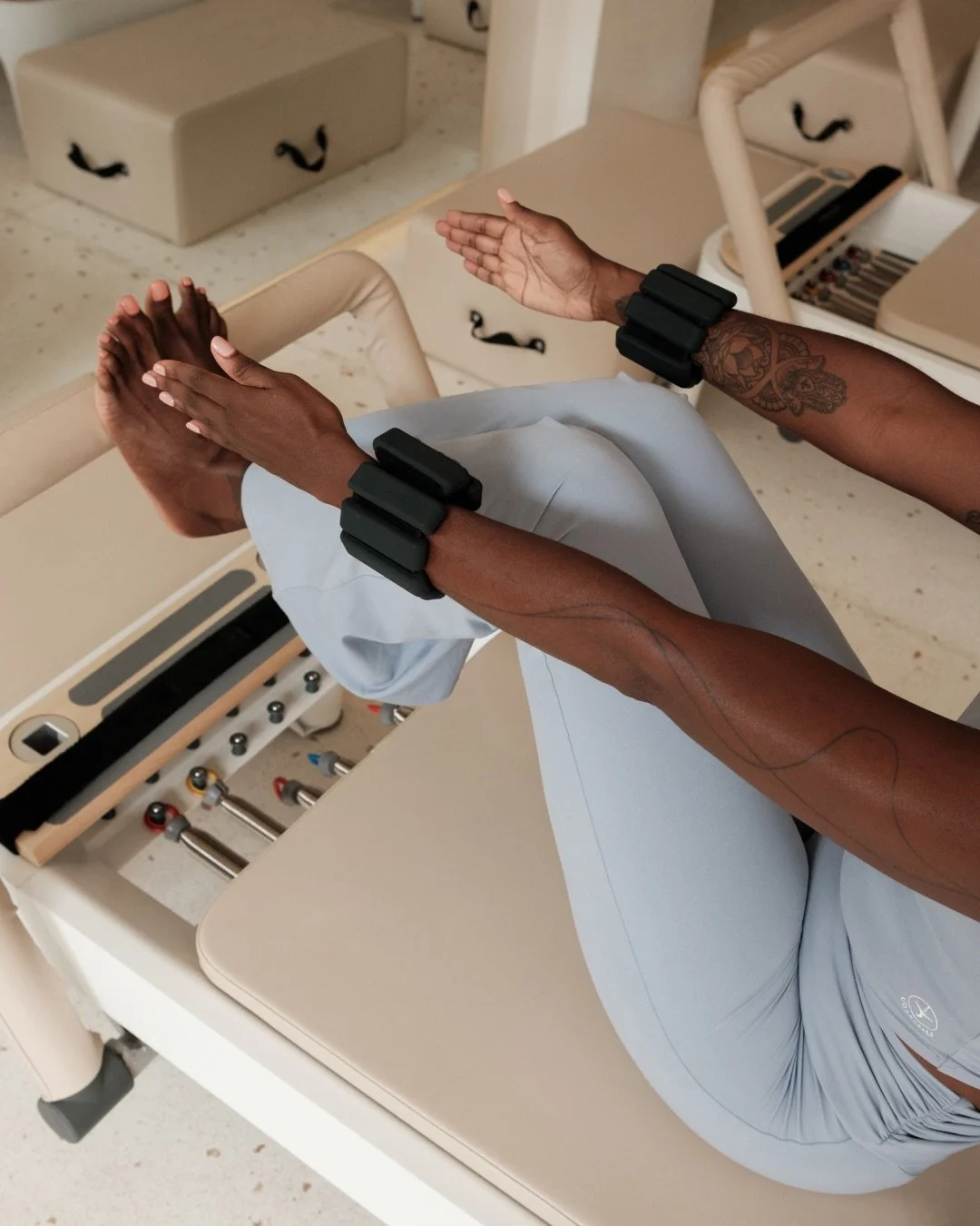 Pilates practitioner on a reformer with ankle weights, reaching toward feet — recorded Pilates workshops on movement science and studio application