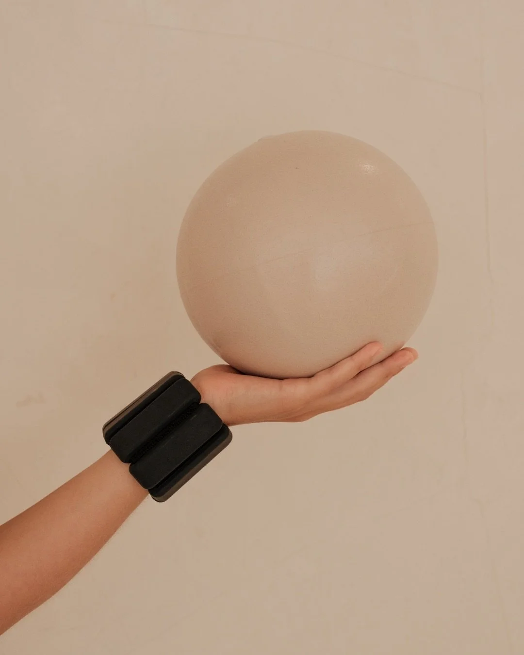 Hand holding a small Pilates ball with wrist weight — targeted Pilates continuing education on cueing, load, and movement adaptation