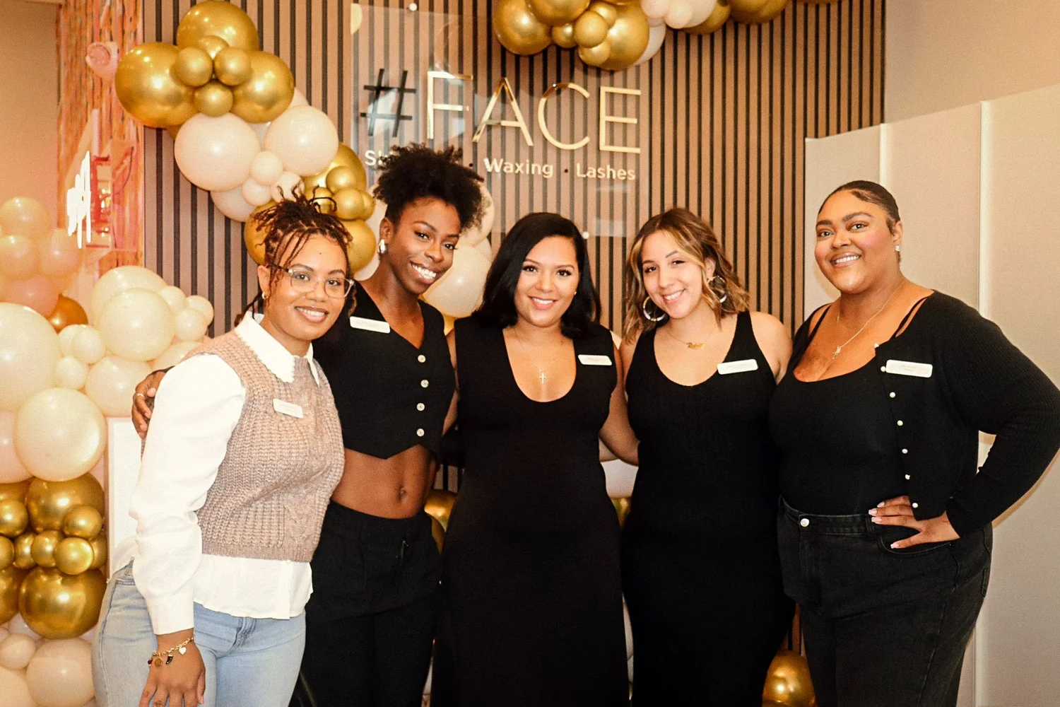Five staff posing before balloons and the #FACE sign