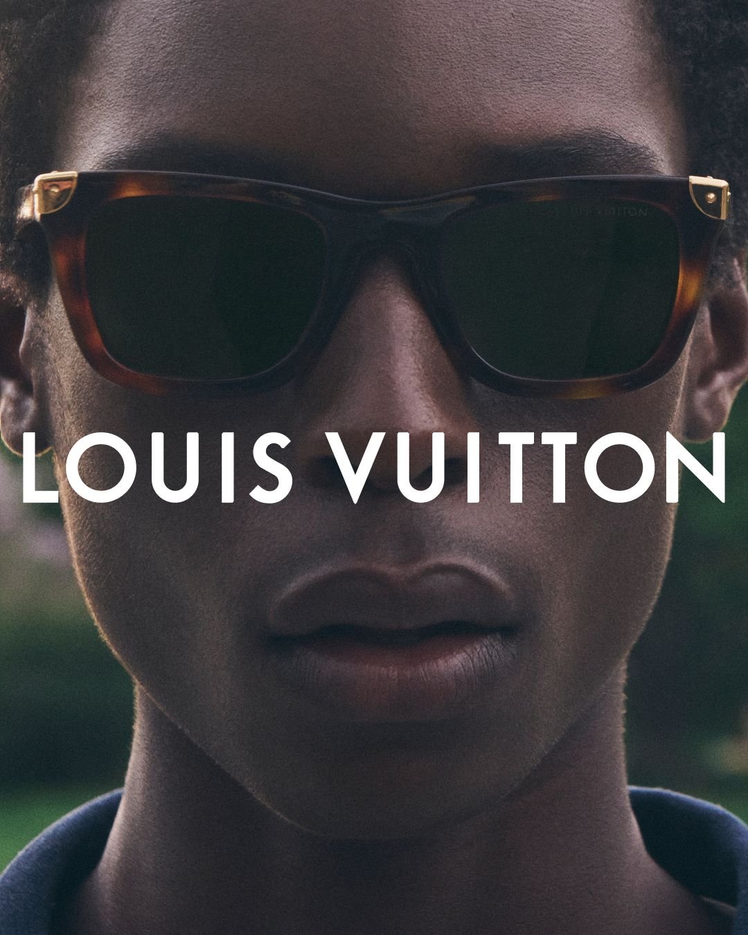 A close-up of a person with dark skin wearing large tortoise-shell sunglasses, with the Louis Vuitton logo overlaid in white.