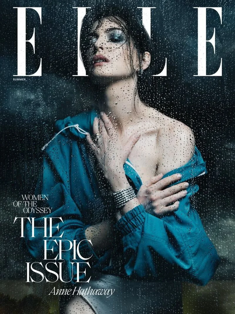 Magazine cover for Elle featuring a woman with wet hair and makeup behind a rain-covered window, wearing a blue rain jacket, with text indicating it's the summer issue and titled 'Women of the Odyssey: The Epic Issue' by Anne Hathaway.