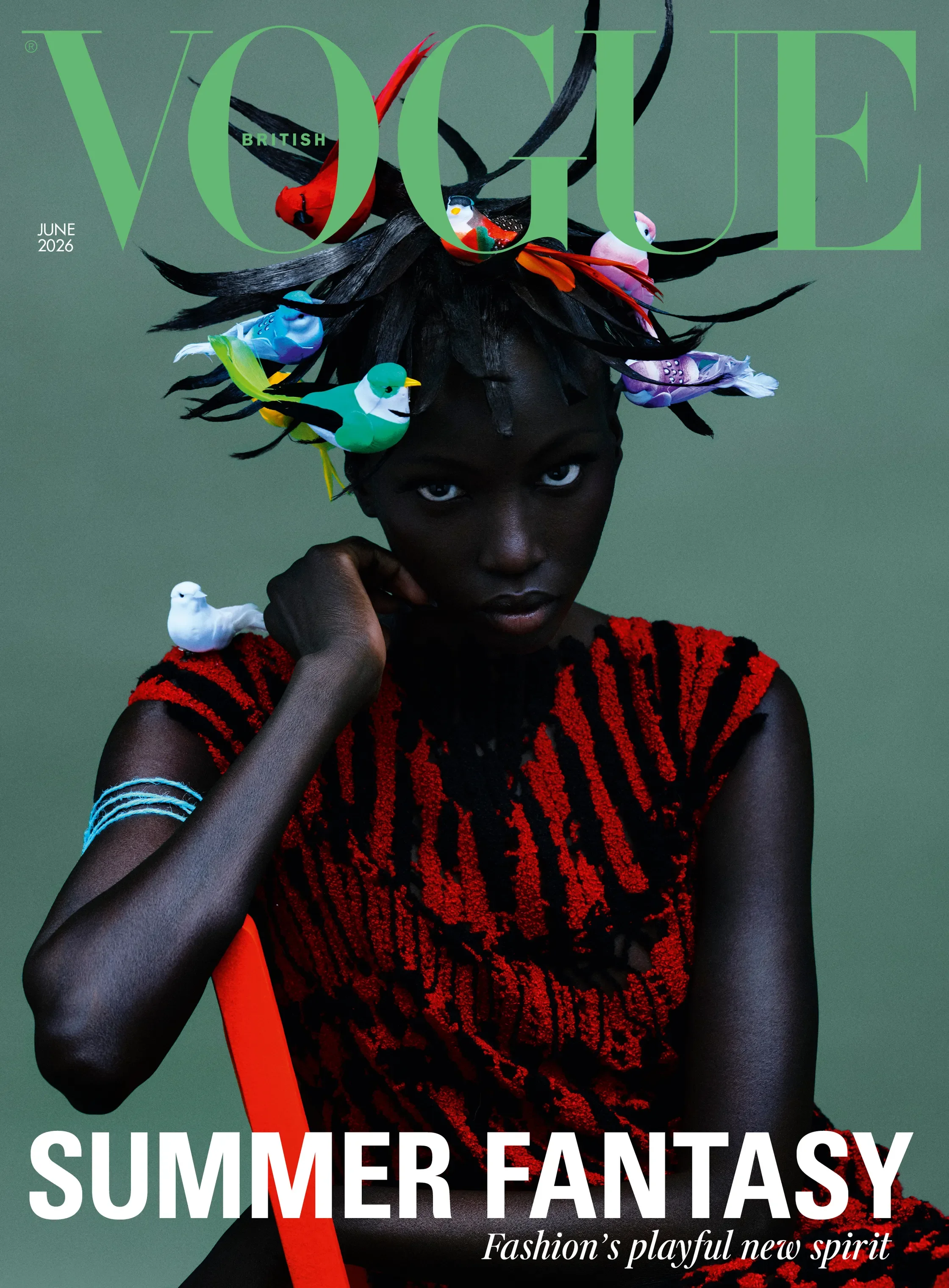 Fashion magazine cover featuring a woman with dark skin and white eyes, wearing a red and black textured dress, with hair decorated as a crown made of colorful toy birds. The magazine name is Vogue British, June 2026 issue, with headlines about summer fashion and playful spirit.