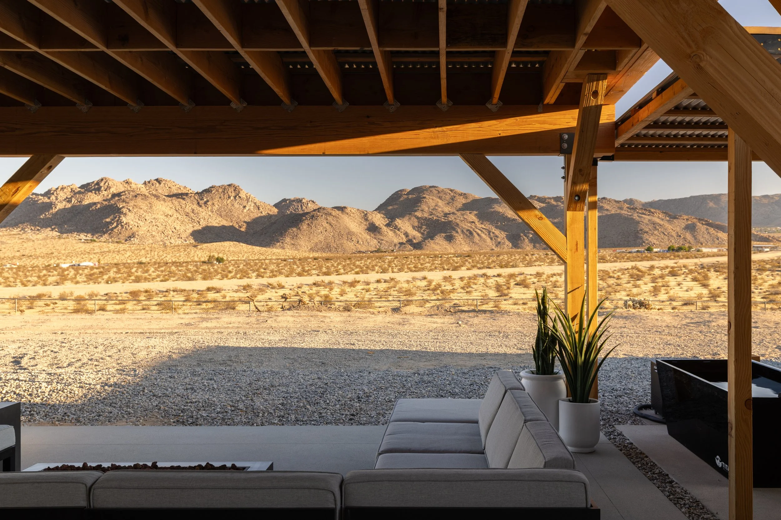 Modern outdoor patio with gray cushioned seating and potted plants, overlooking a desert landscape with mountains in the distance