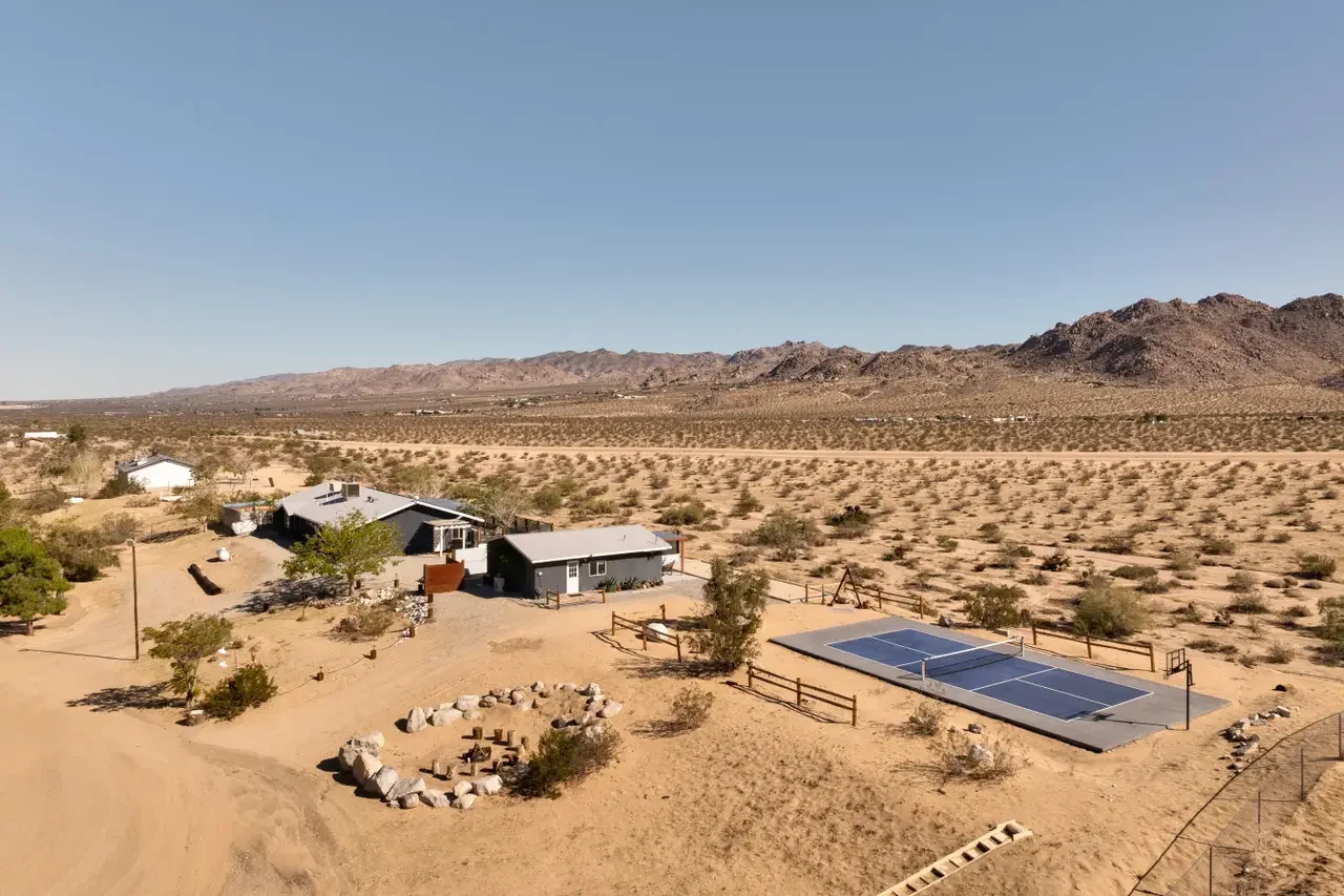 A desert property with a house, solar panels, surrounded by arid land with sparse vegetation and mountains in the background.