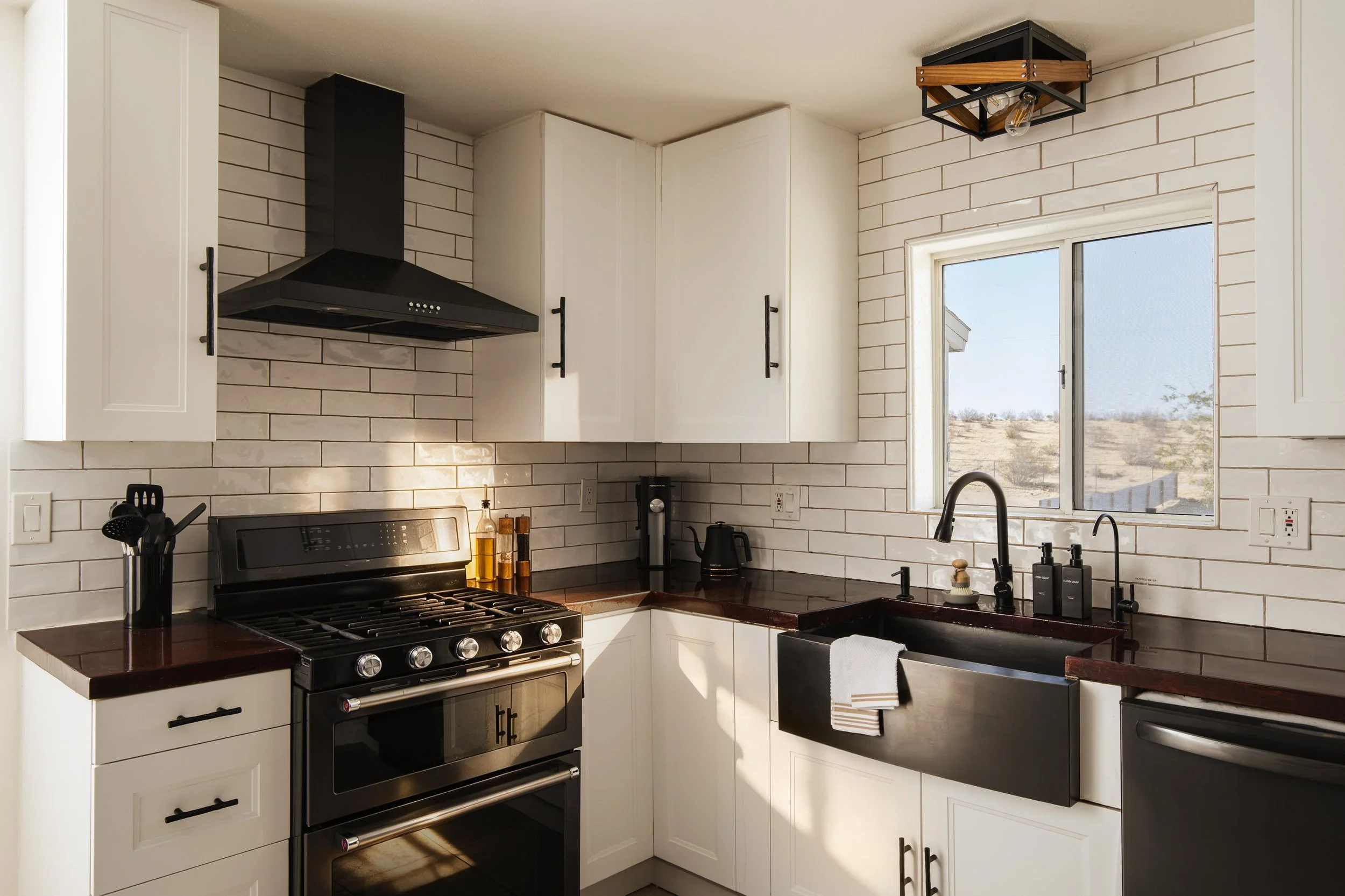 A modern kitchen with white cabinets, a stainless steel stove, black countertops, and a window looking outside