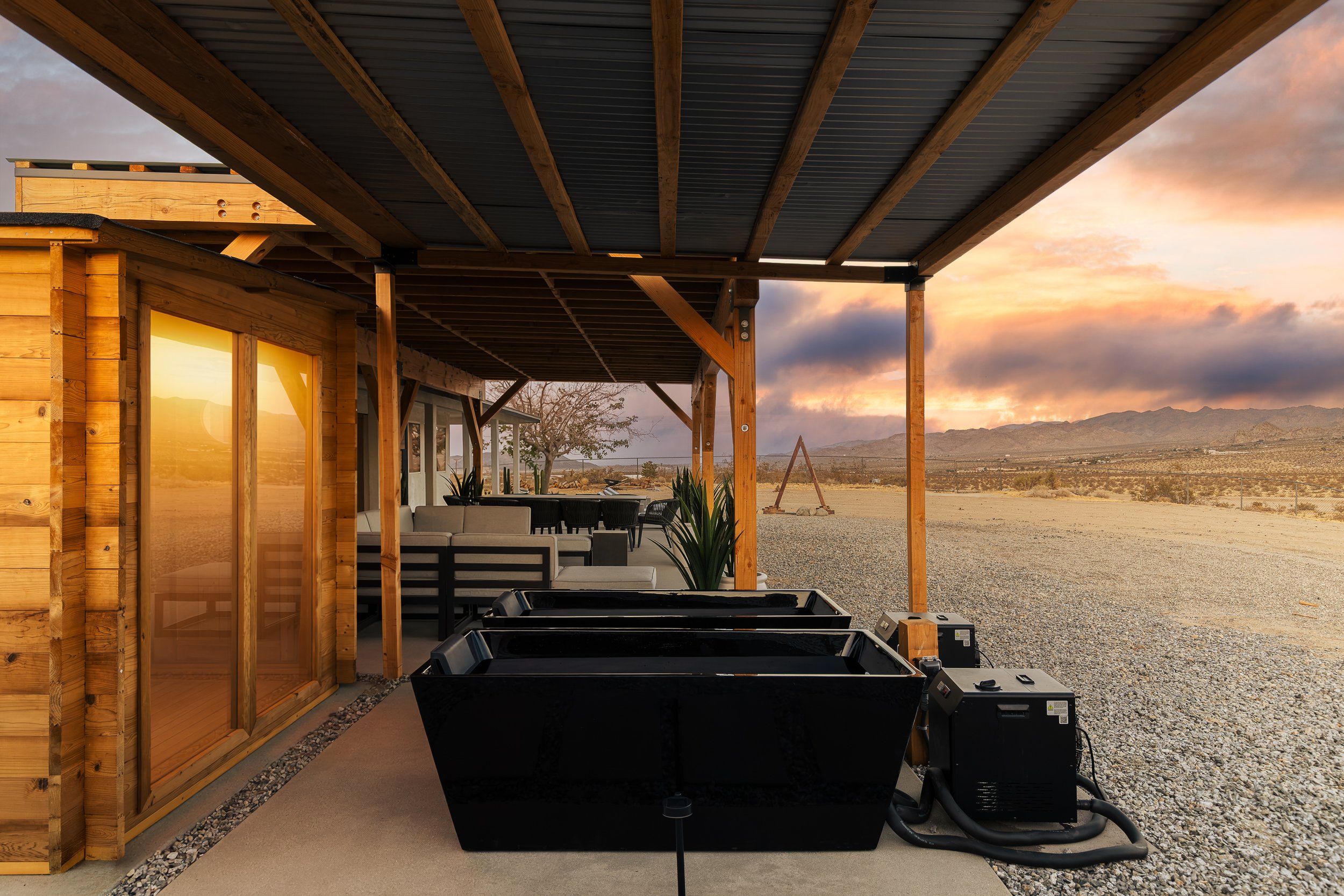 Outdoor deck area with seating, railing, and a hot tub in a desert landscape during sunset, with mountains in the background.