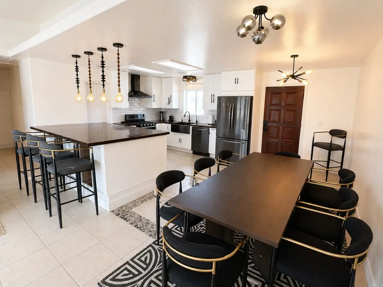 Modern kitchen with black and white cabinetry, an island with a dark wood countertop, pendant lights, and a dining area with a black table and black chairs with gold accents.
