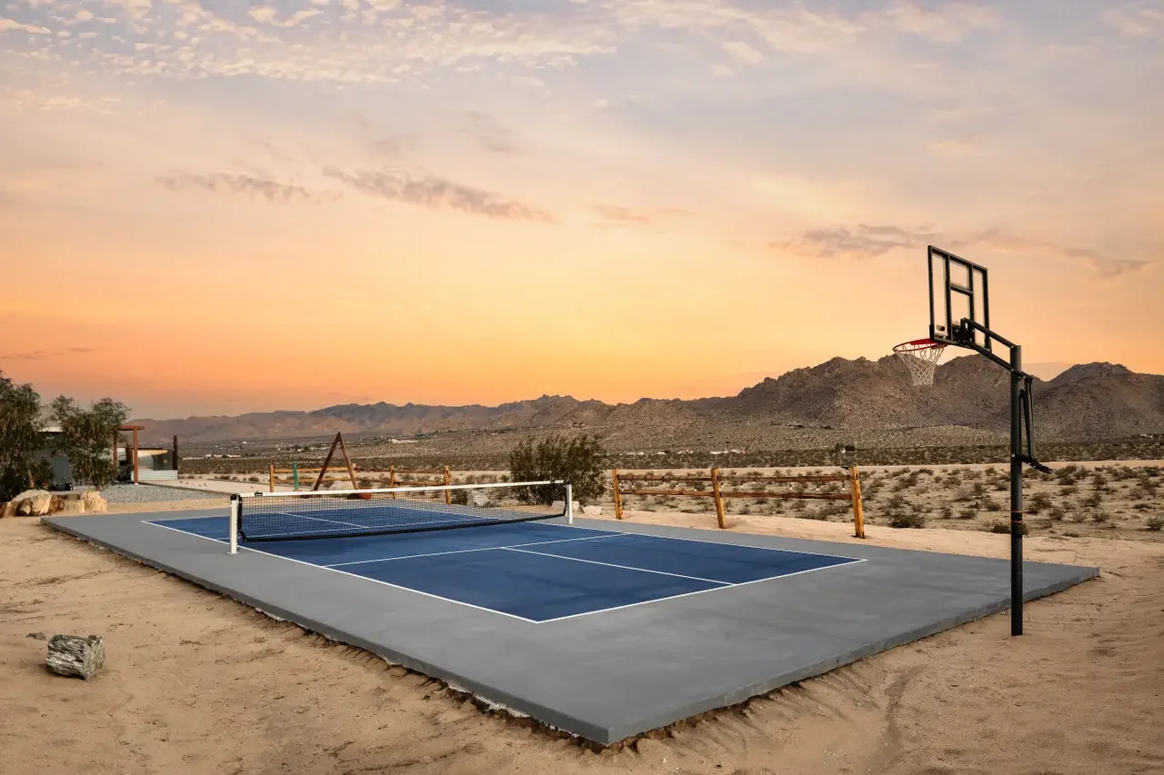 Outdoor set of a tennis court and a basketball hoop against a sunset sky and mountain landscape.