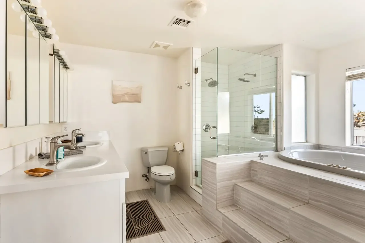 Bathroom with dual sinks, a shower with glass enclosure, a bathtub, and large windows with blinds