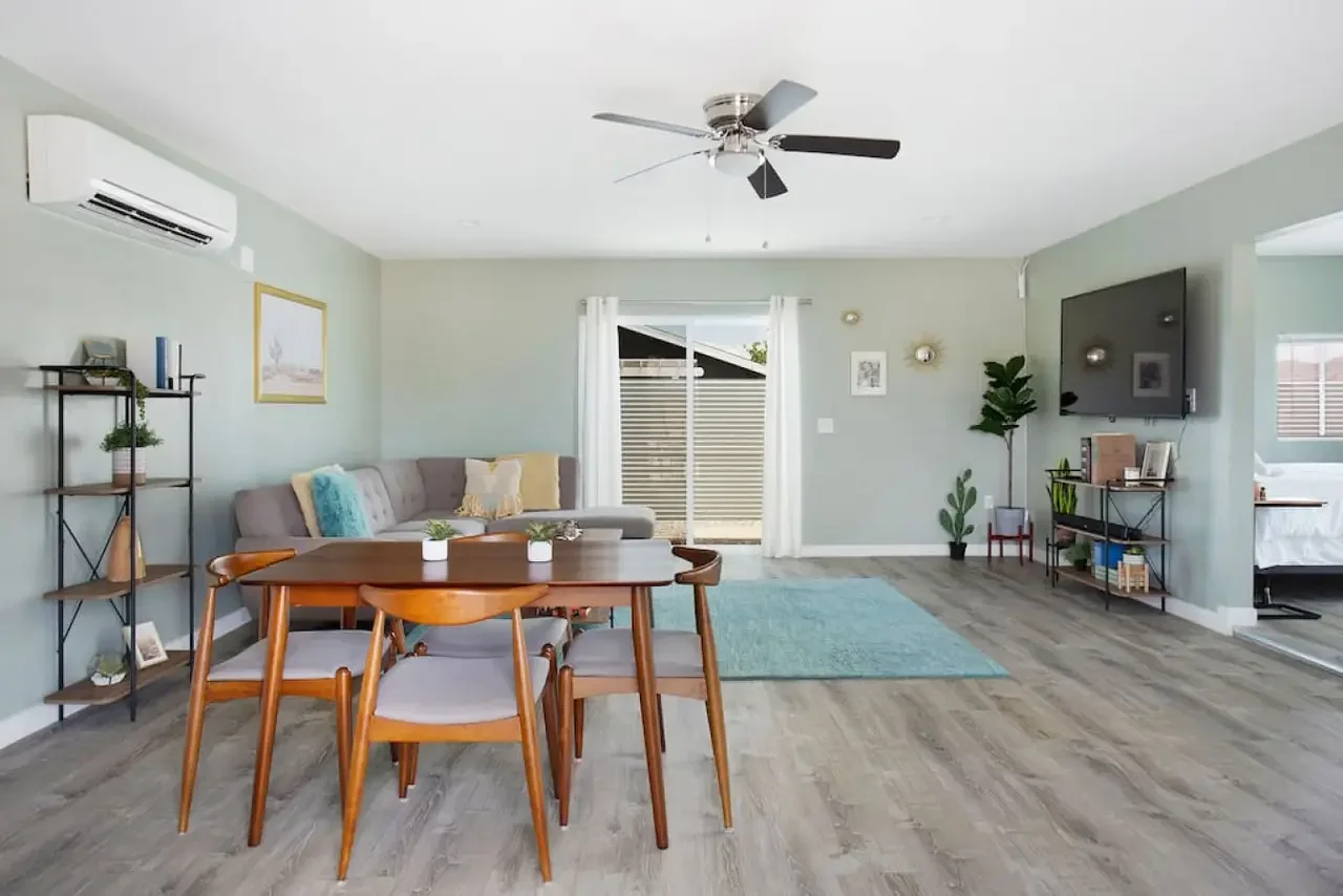 Living room with a dining table, gray sofa, wall-mounted TV, and bamboo flooring.