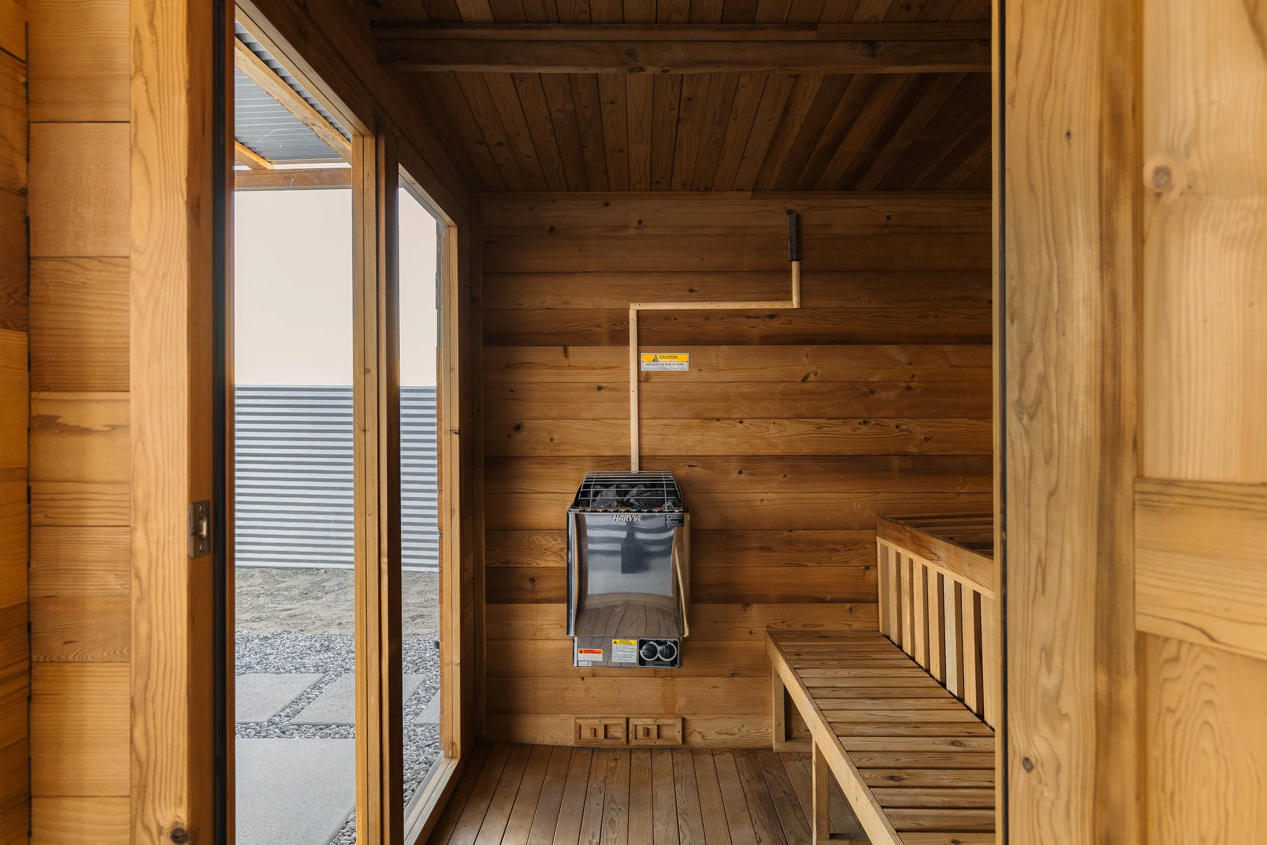 Interior of a wooden sauna room with benches and a heater, viewed through an open doorway.