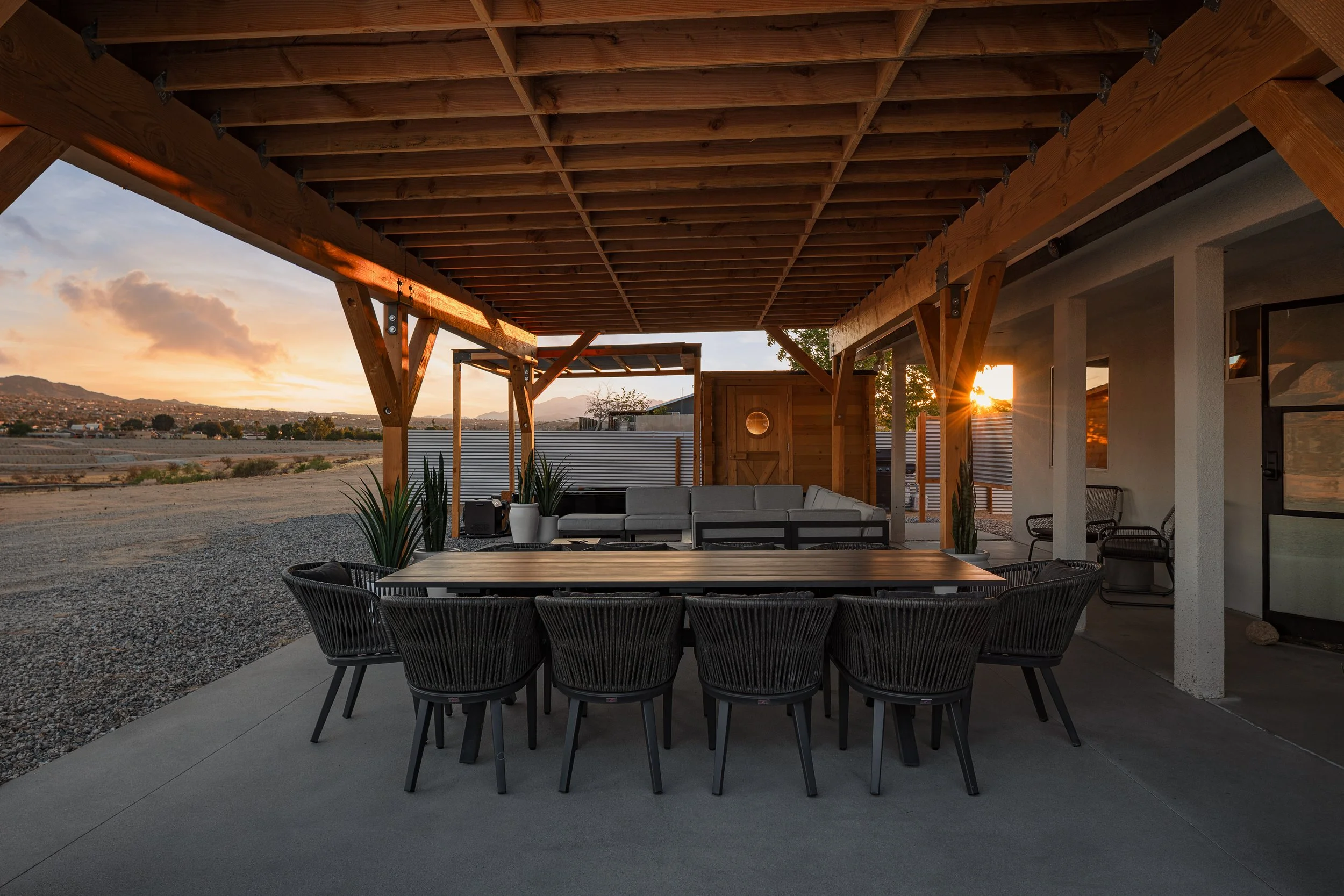 Backyard patio with outdoor seating under a wooden pergola during sunset, with mountain view in the background.