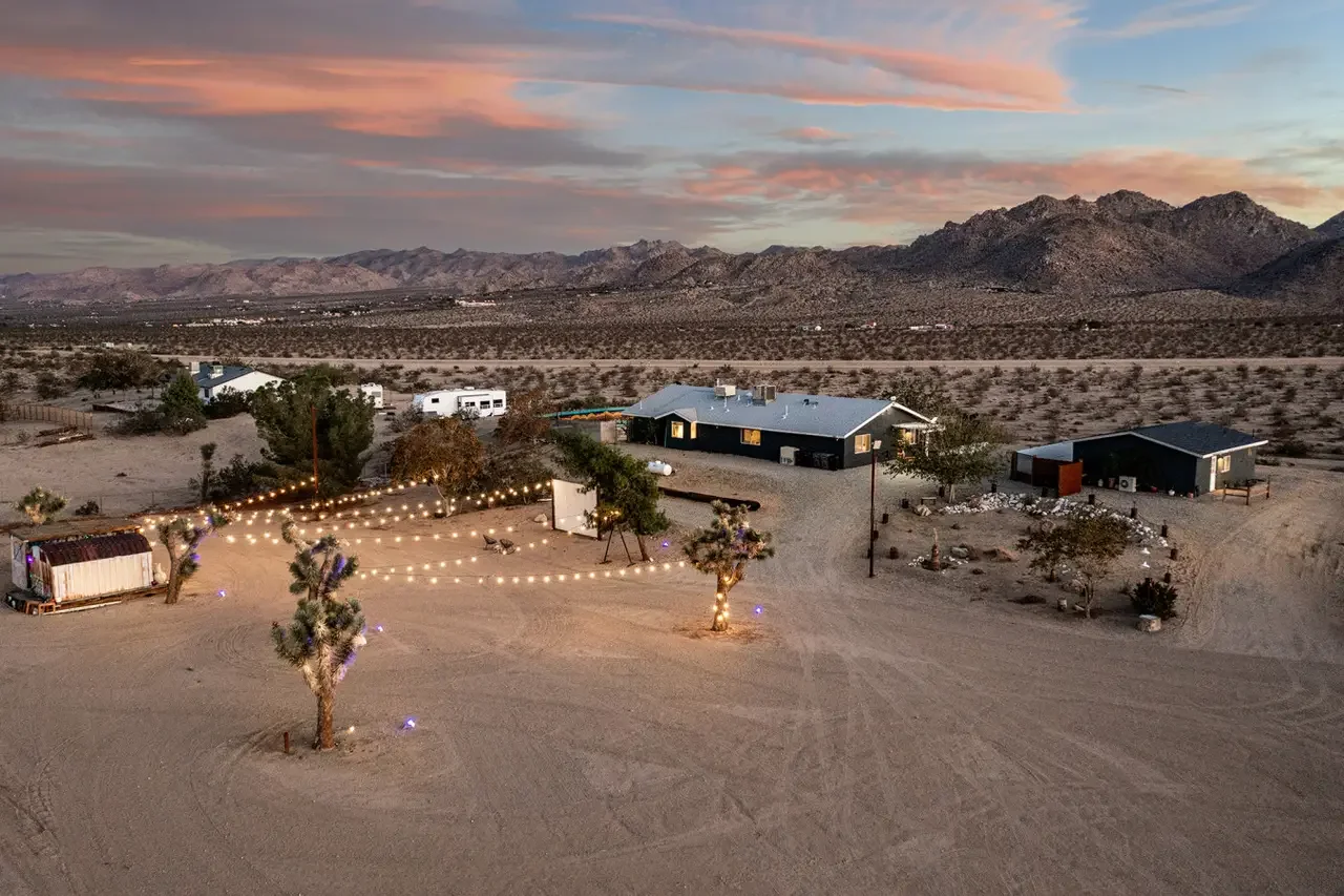 Aerial view of a desert landscape at sunset with a few houses and string lights decorated outdoor area.