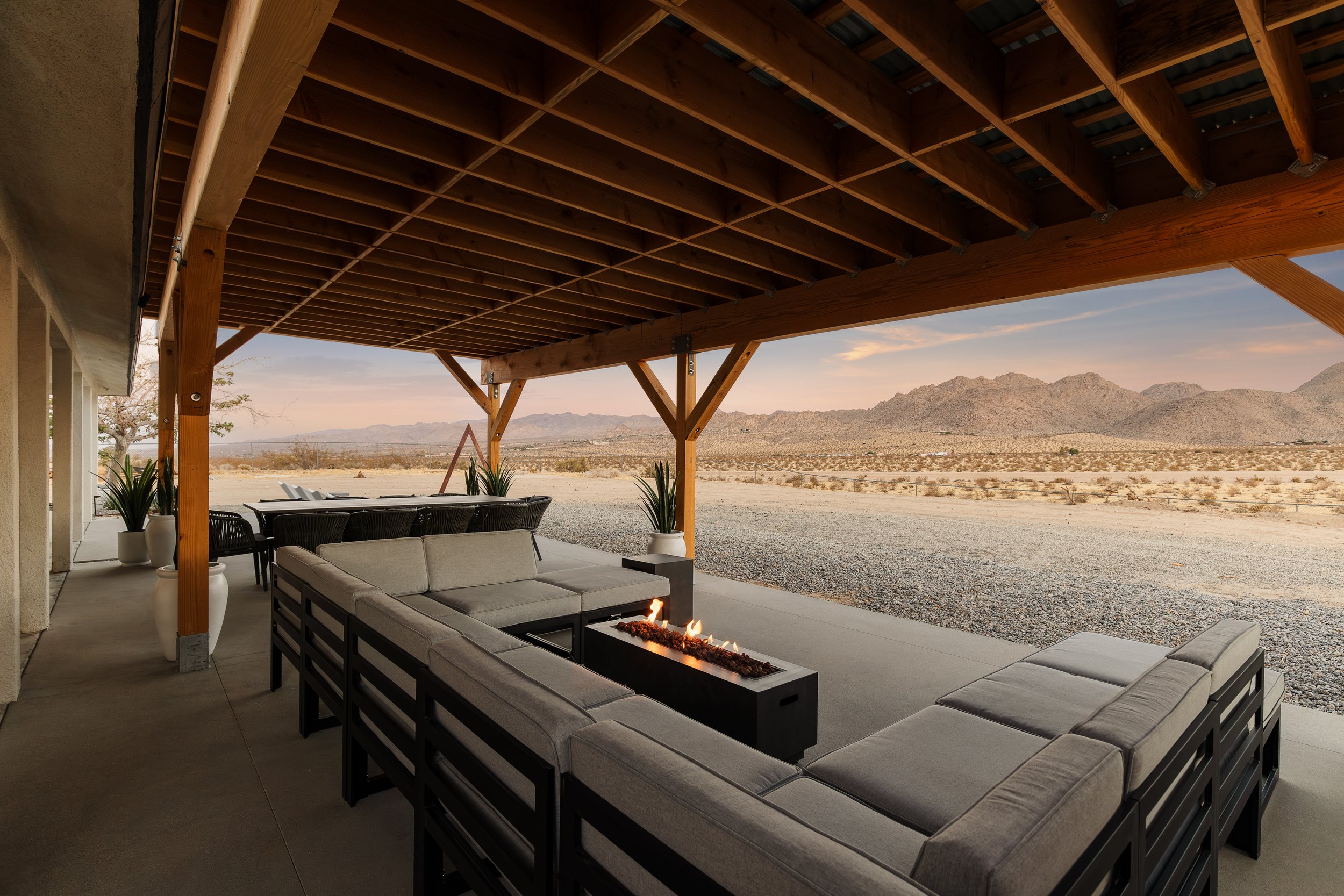 A covered outdoor patio with a seating area, fire pit, and mountain view in the background.