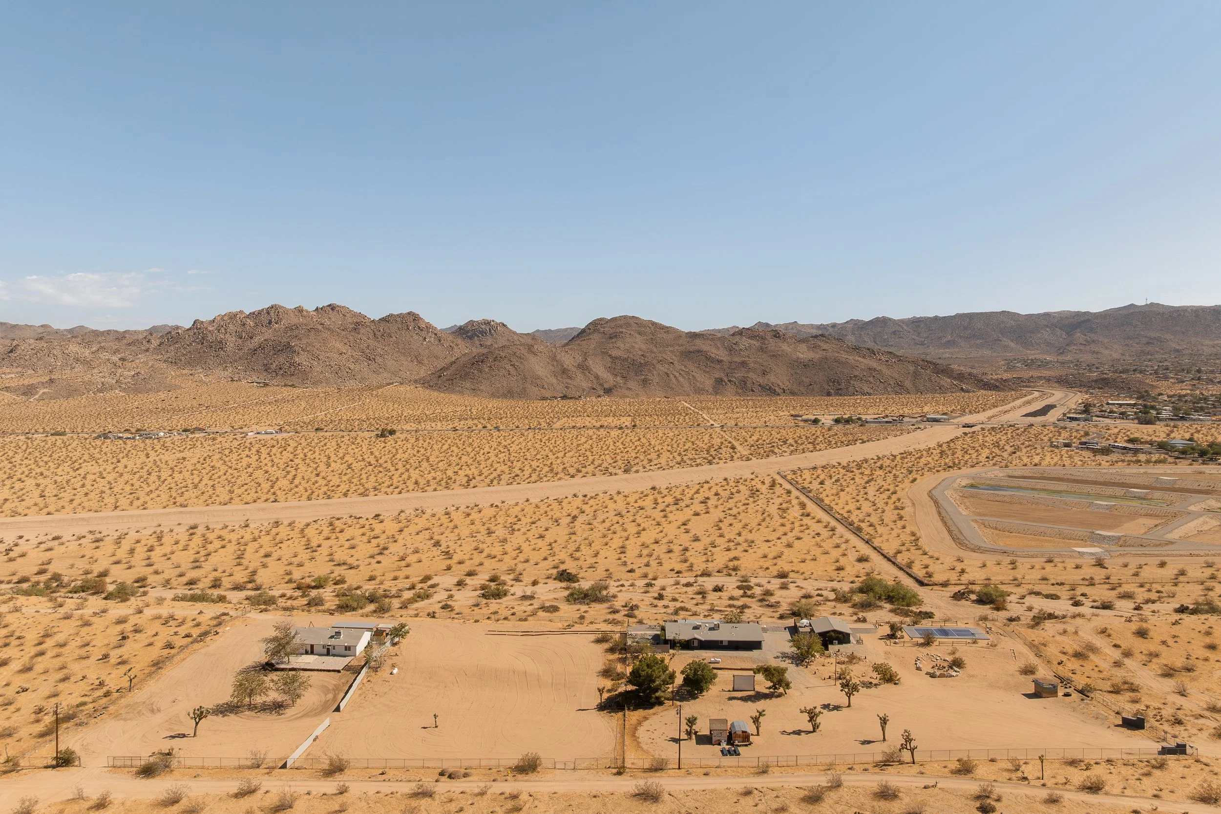 A desert landscape with mountains in the background, sparse vegetation, and a few residential buildings and structures.