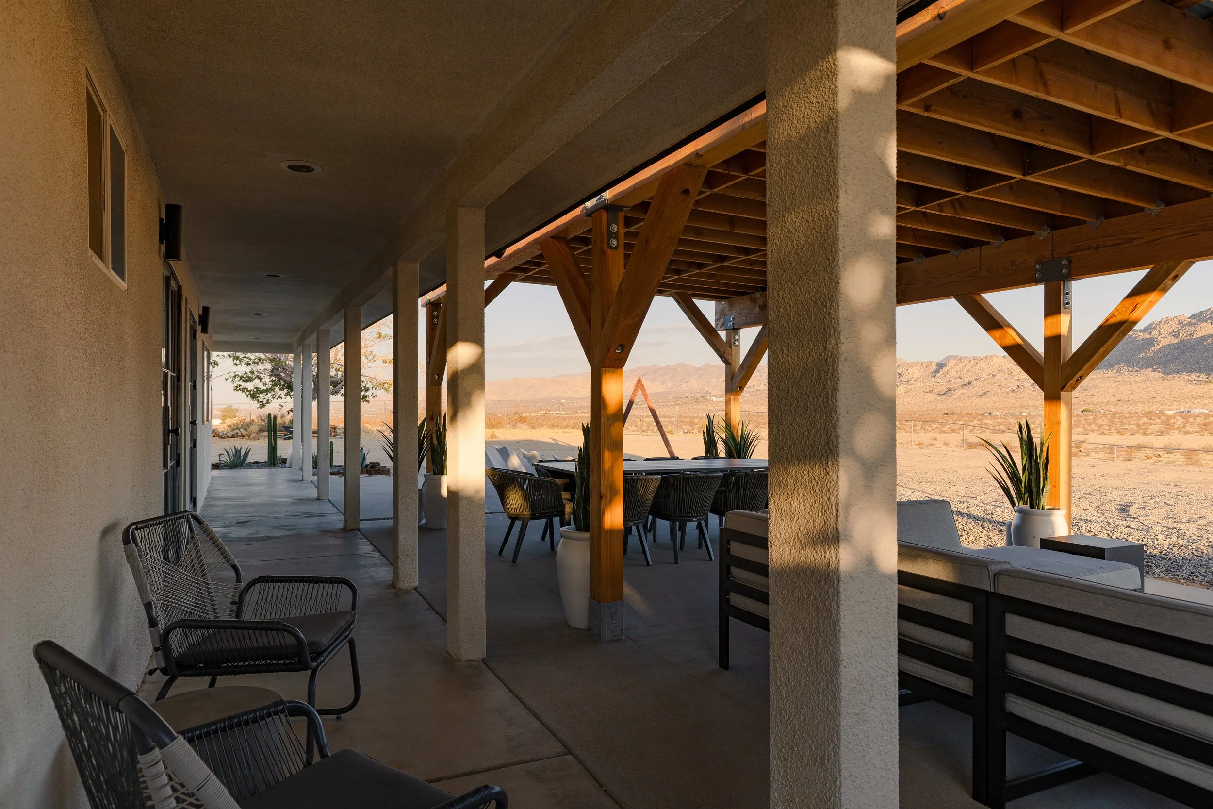 Outdoor patio with tables and chairs, a covered roof area, and a desert landscape with mountains in the background.