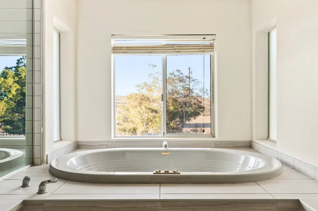 Bathroom with a large bathtub positioned beneath a window showing trees outside.