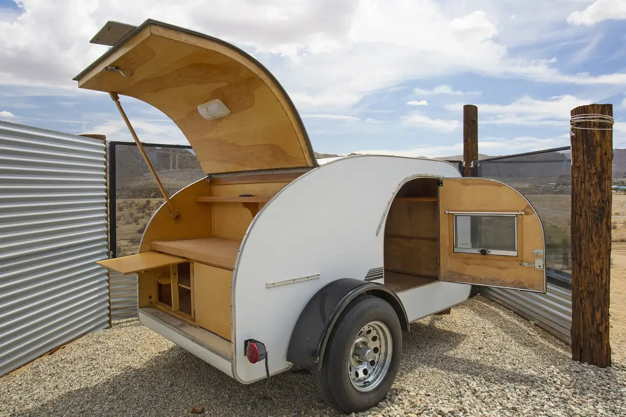 Small portable truck with open sides and interior storage, parked in a desert area with a metal fence and wooden posts.